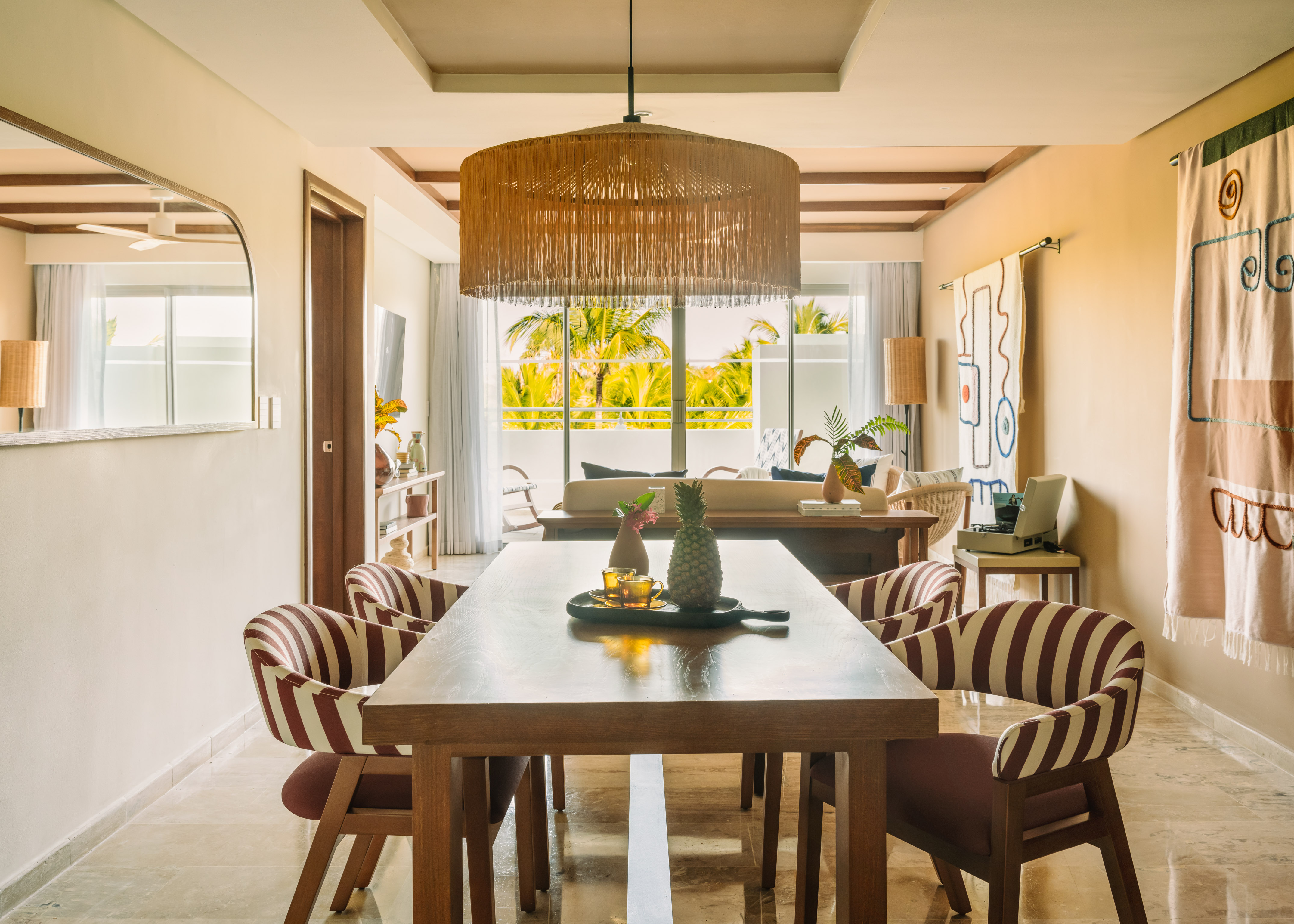Tropical dining room with modern table, striped chairs, and palm tree views.