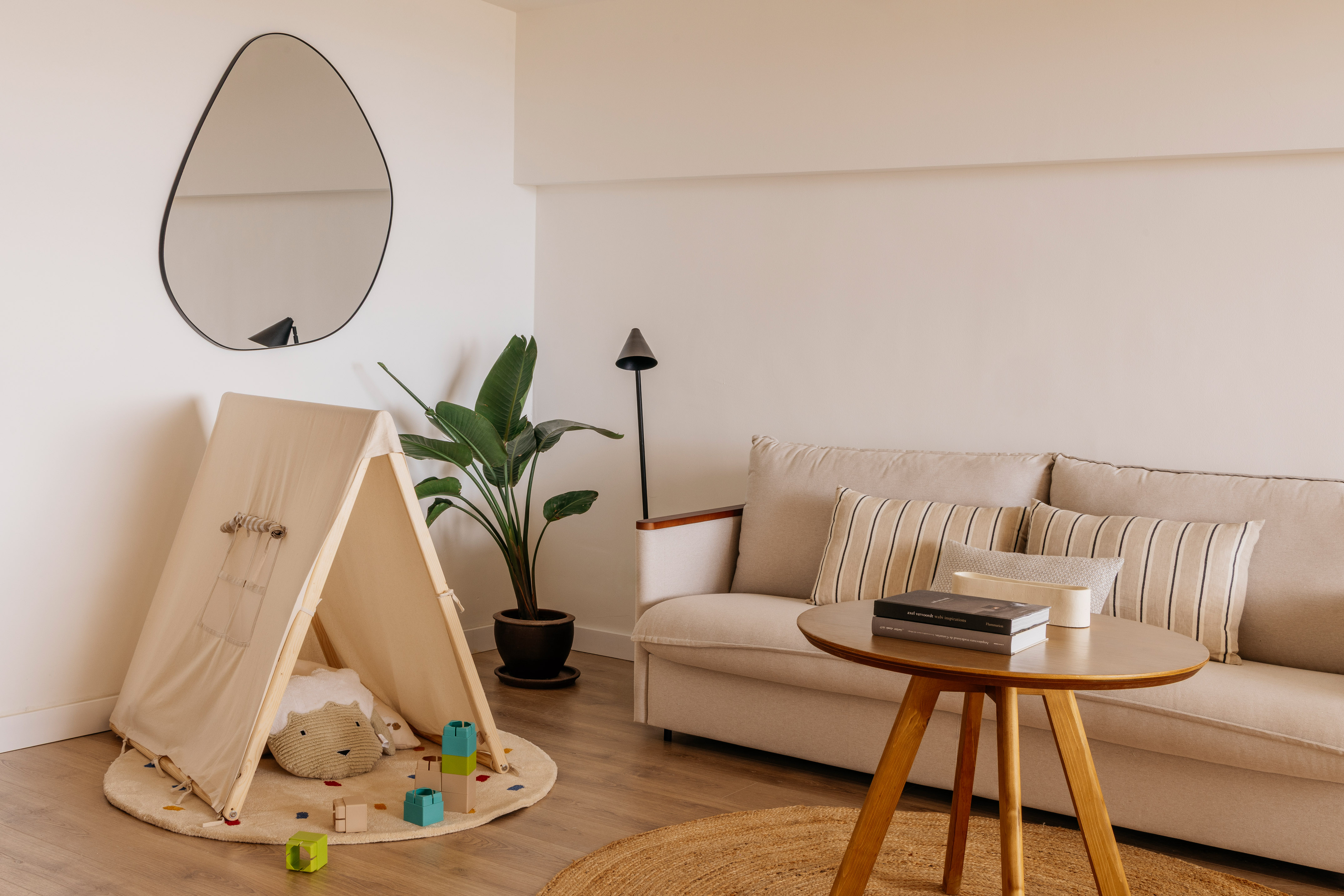 Modern living room with beige sofa, kids' teepee, plant, and minimalist decor.