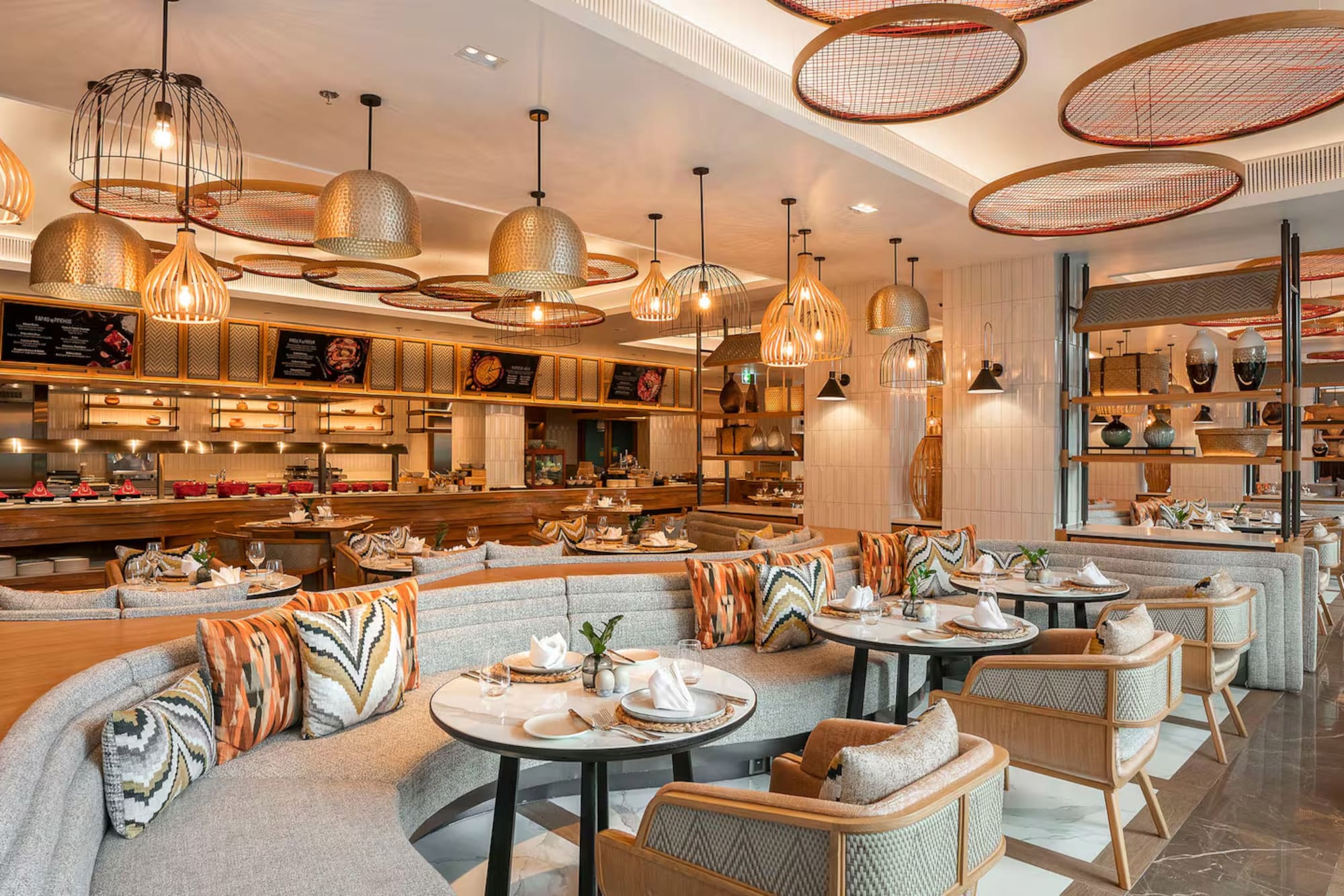 Modern restaurant interior with open kitchen, buffet dining, stylish seating, and decorative lights.