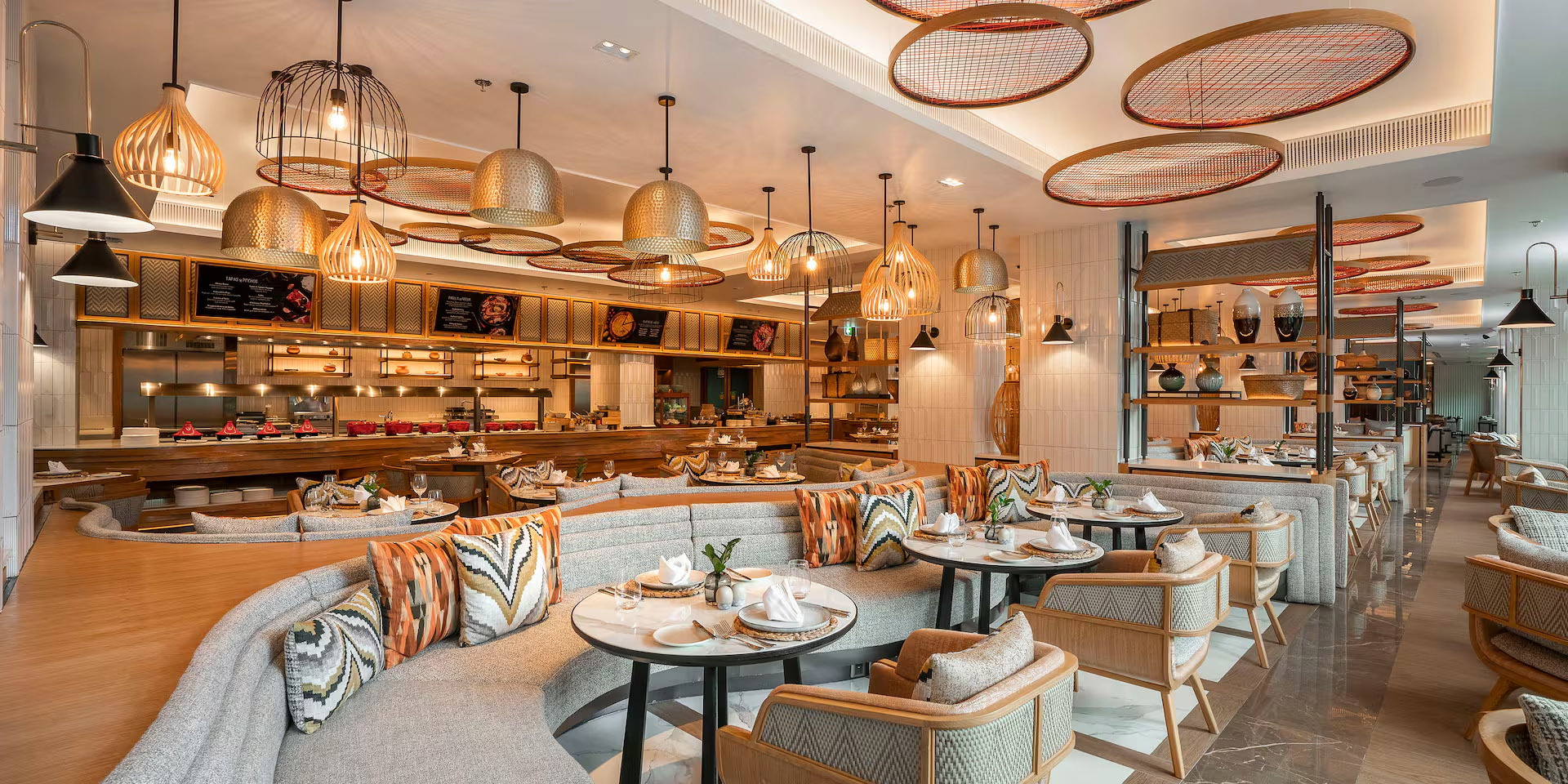 Modern restaurant interior with open kitchen, buffet dining, stylish seating, and decorative lights.