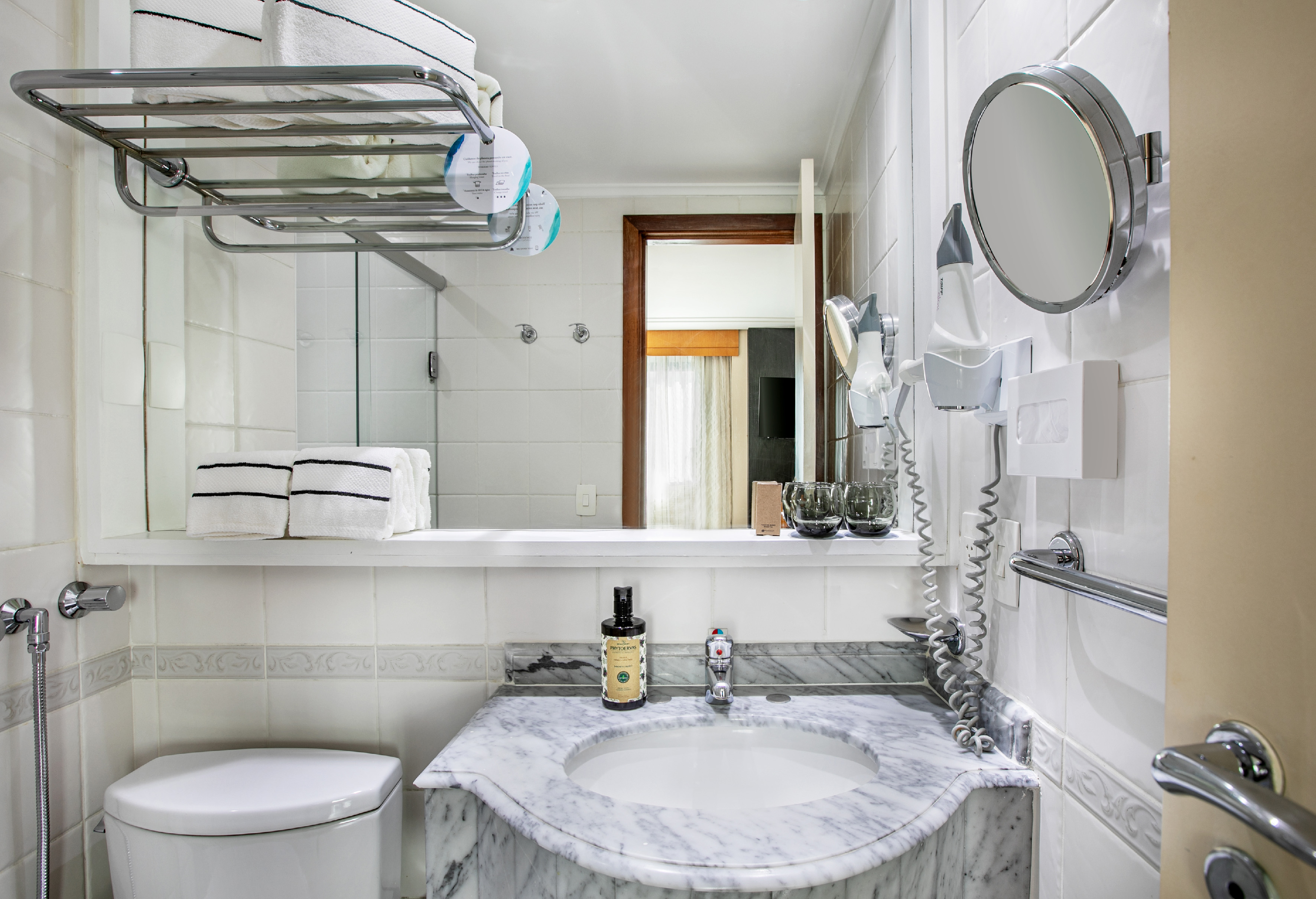 Modern hotel bathroom with marble vanity, sink, toilet, towels, and hairdryer.
