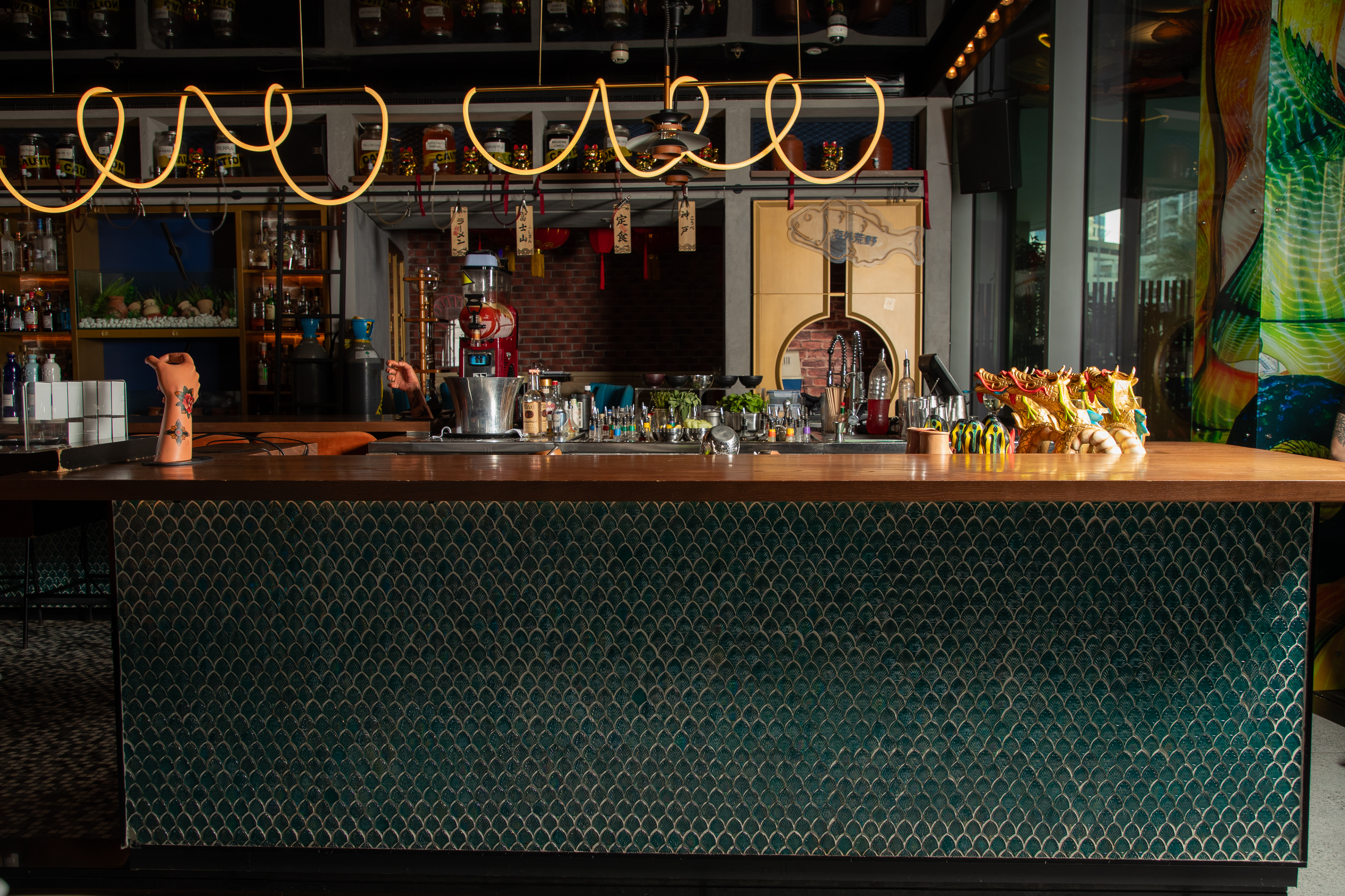 Asian-themed bar interior with teal tile counter, neon light, and drink bottles.