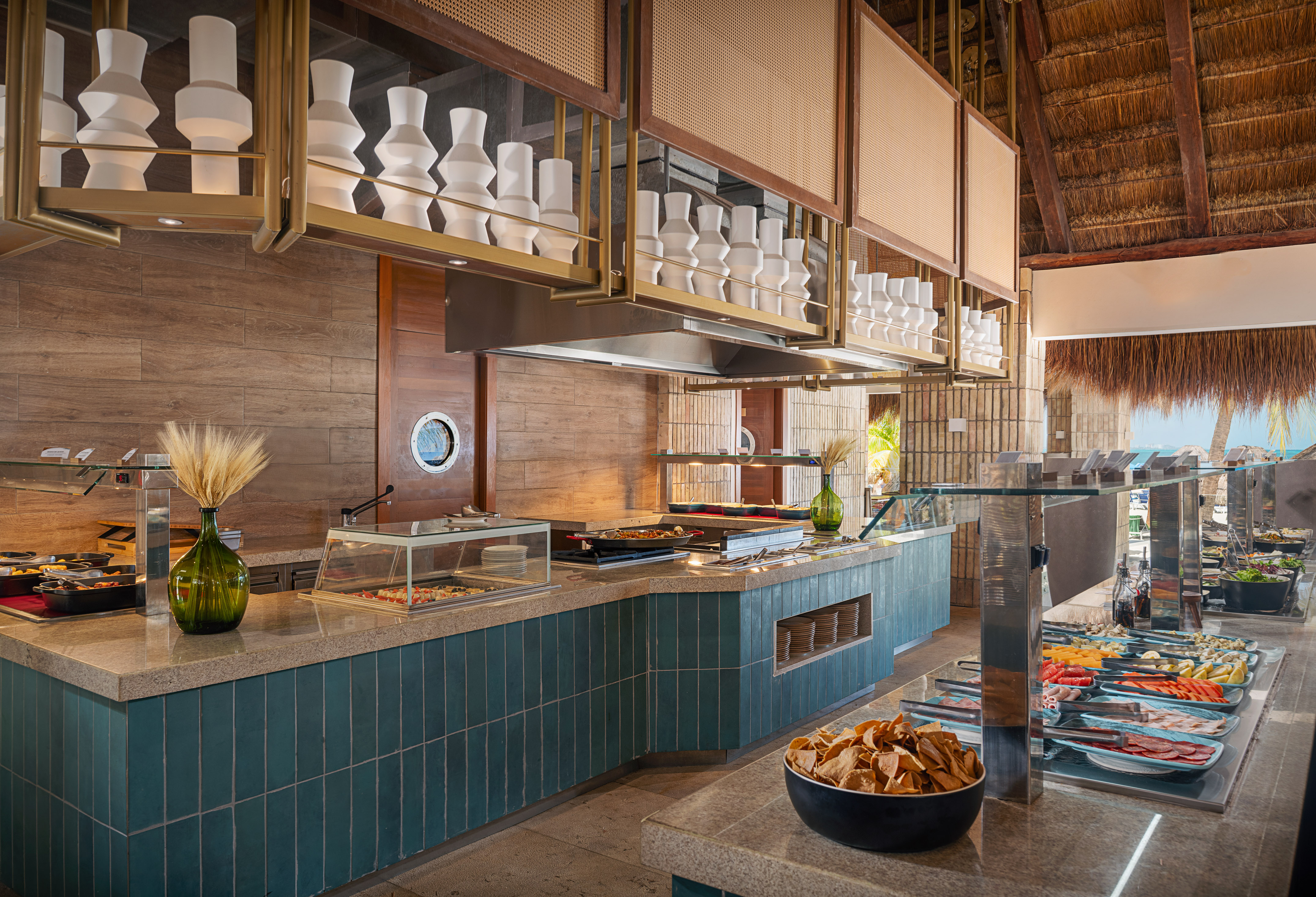 Tropical buffet with diverse food stations, teal counter, and thatched roof.