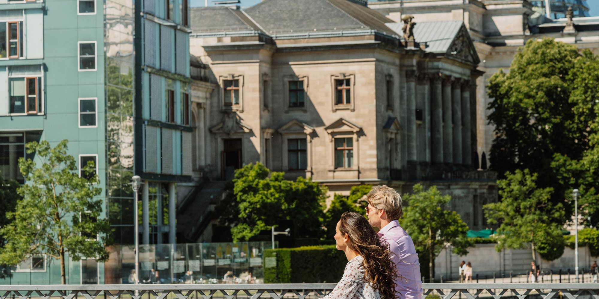 Cycling couple on Berlin bridge with Reichstag dome.