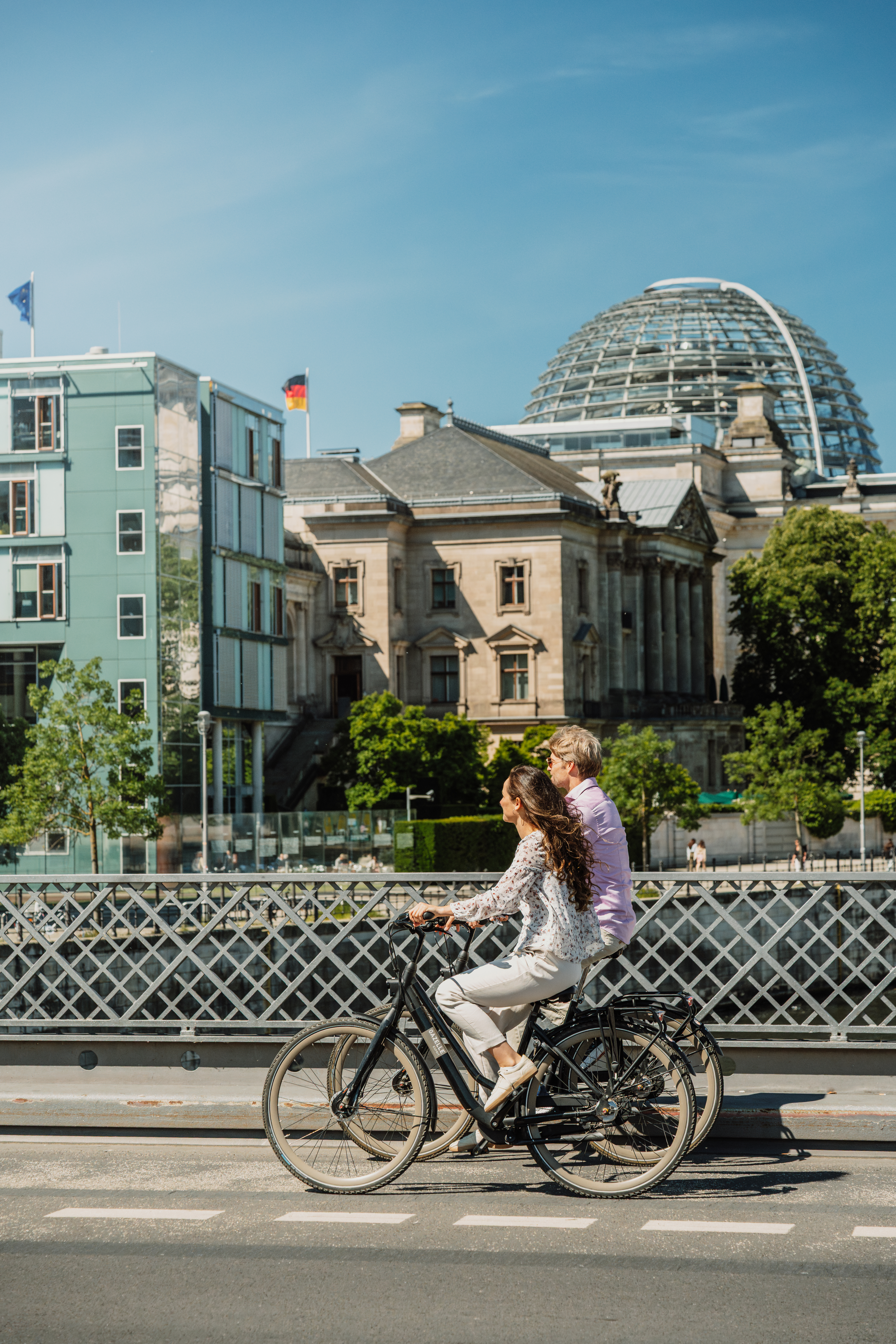 Cycling couple on Berlin bridge with Reichstag dome.