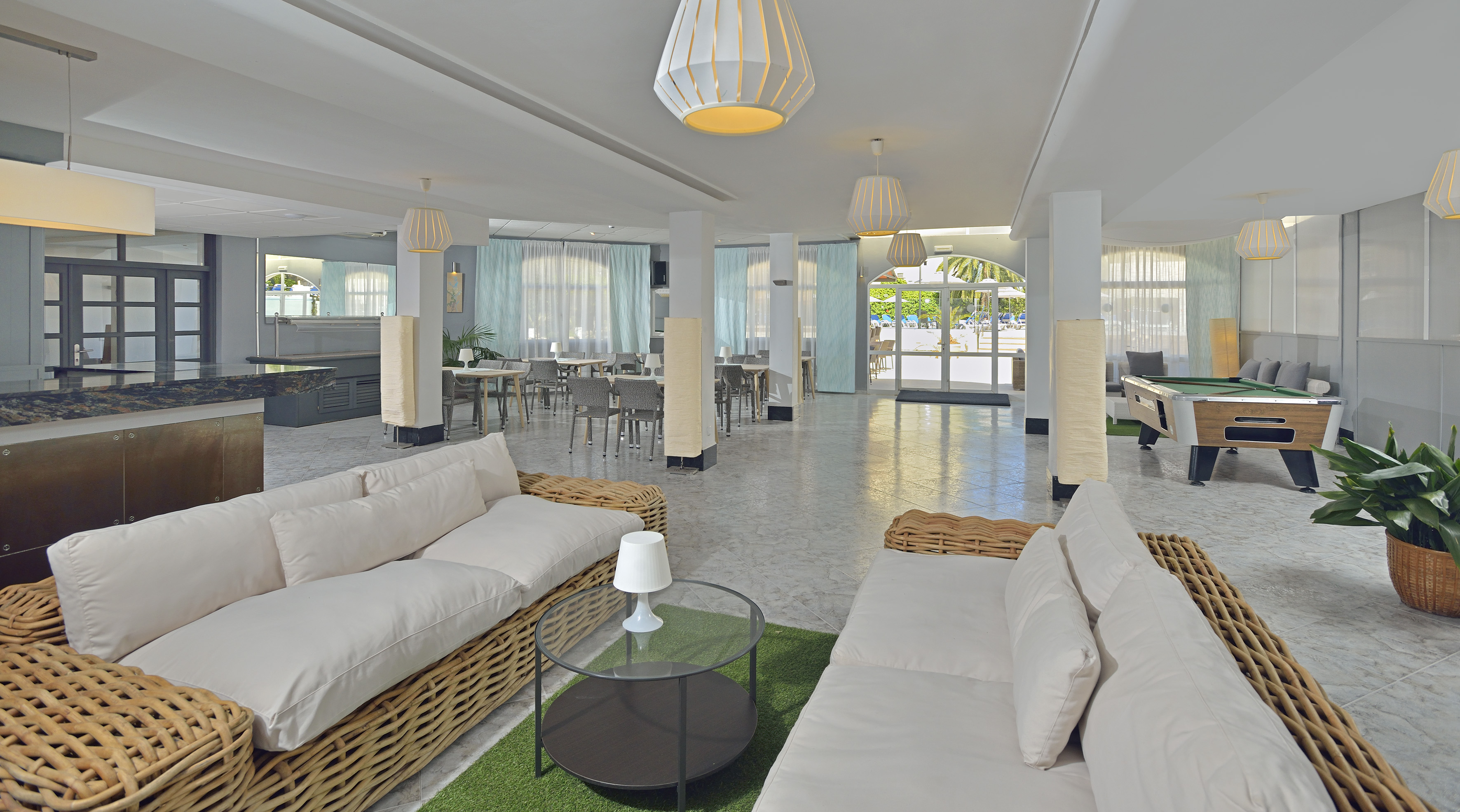 Spacious resort lounge with wicker sofas, dining area, bar, and pool table.