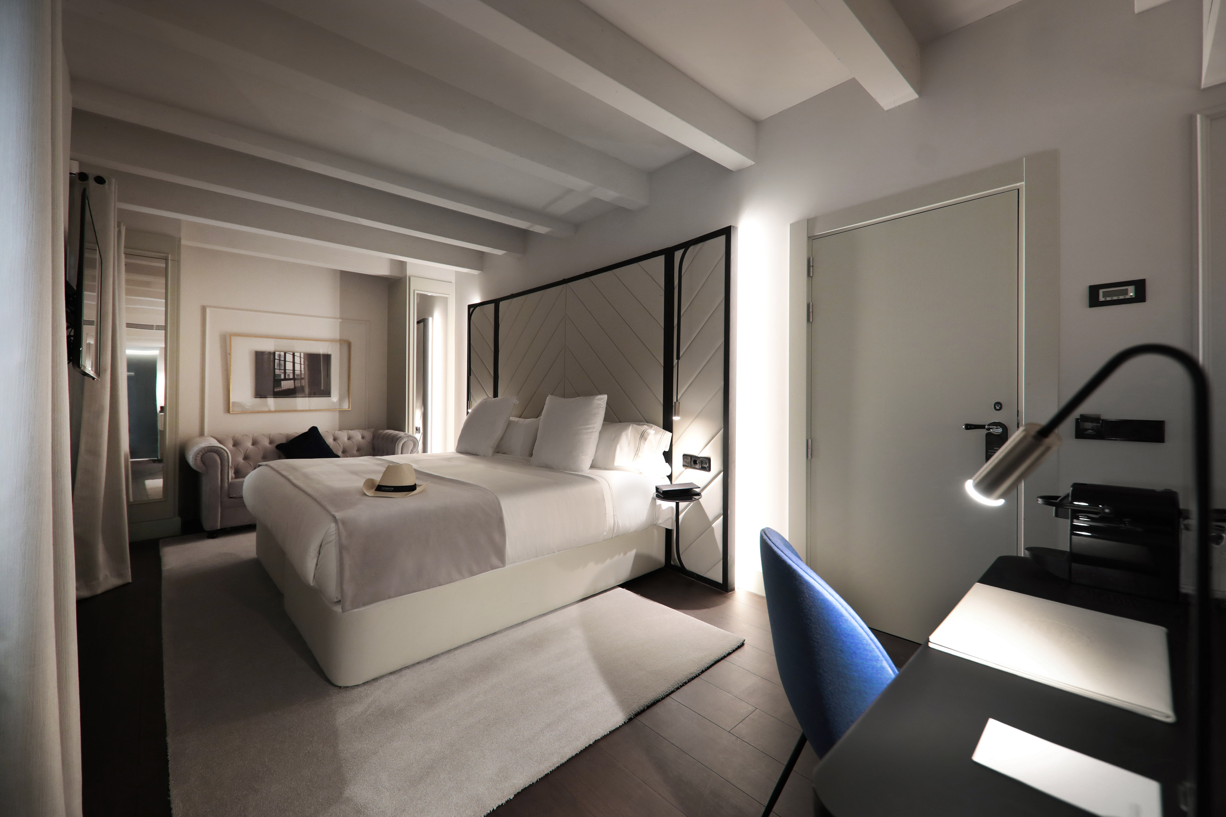 Modern hotel bedroom with large bed, upholstered headboard, desk, and sofa.