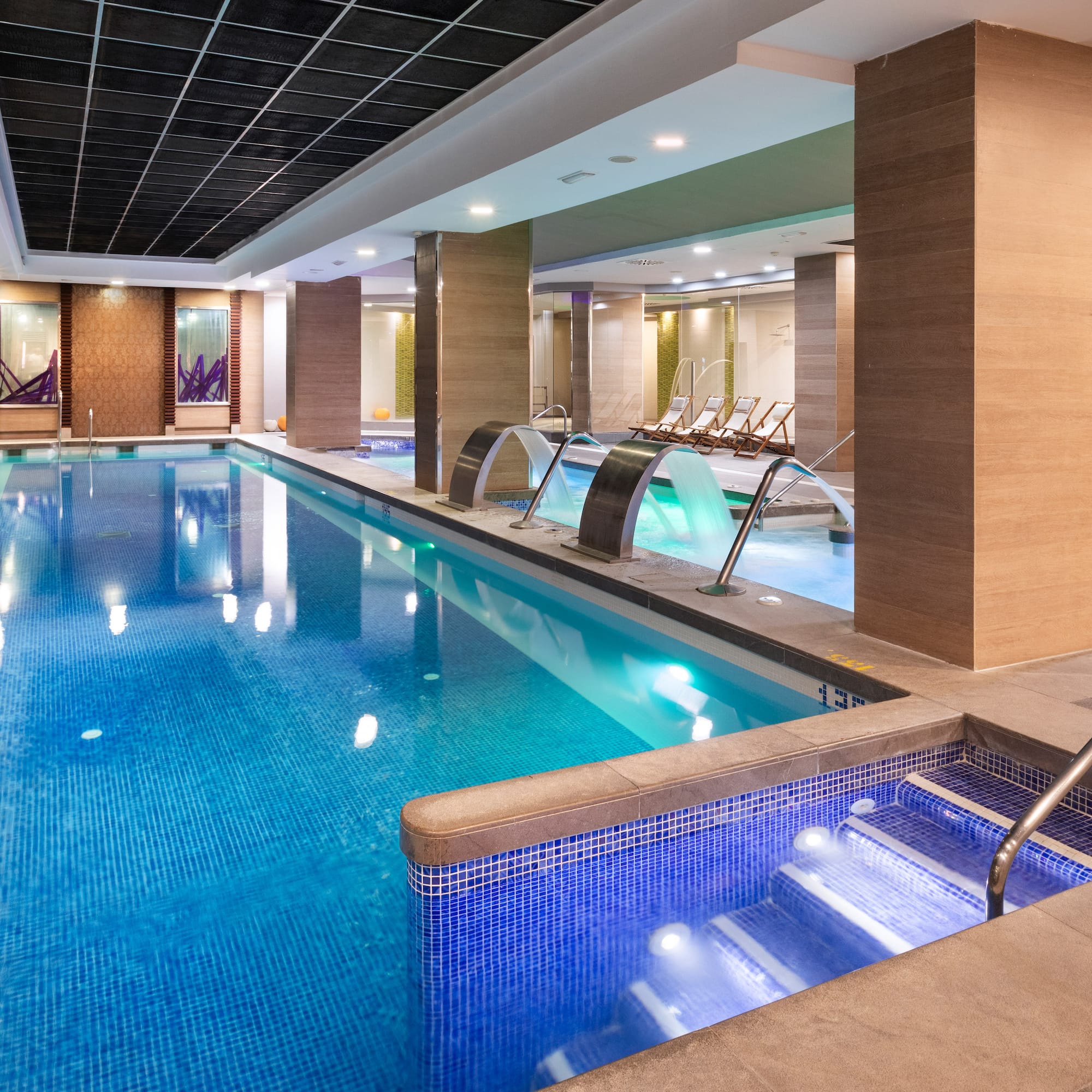 Indoor luxury spa pool with blue mosaic tiles and elegant waterfall features.