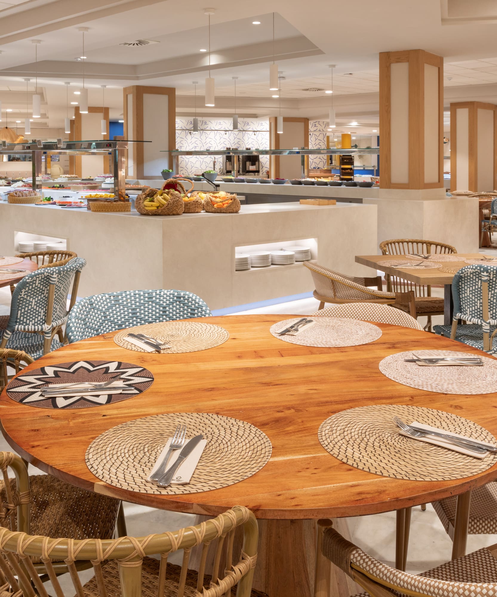 Spacious hotel buffet restaurant with wooden tables and woven chairs.