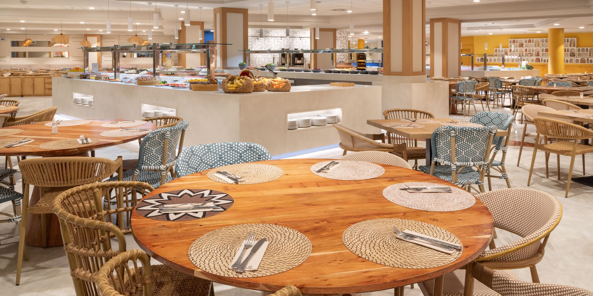 Bright resort buffet restaurant with round wooden tables and varied seating.