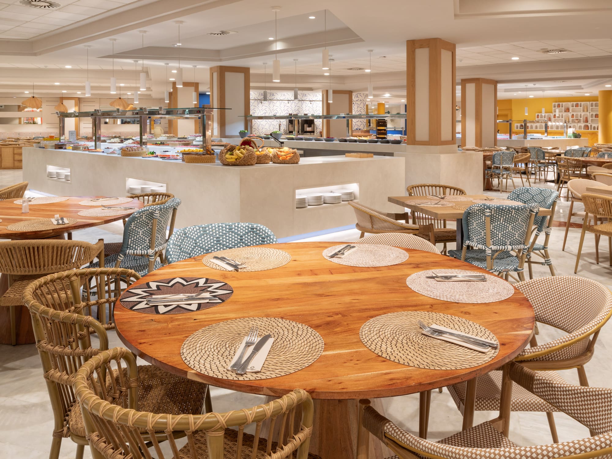 Spacious hotel buffet restaurant with wooden tables and woven chairs.