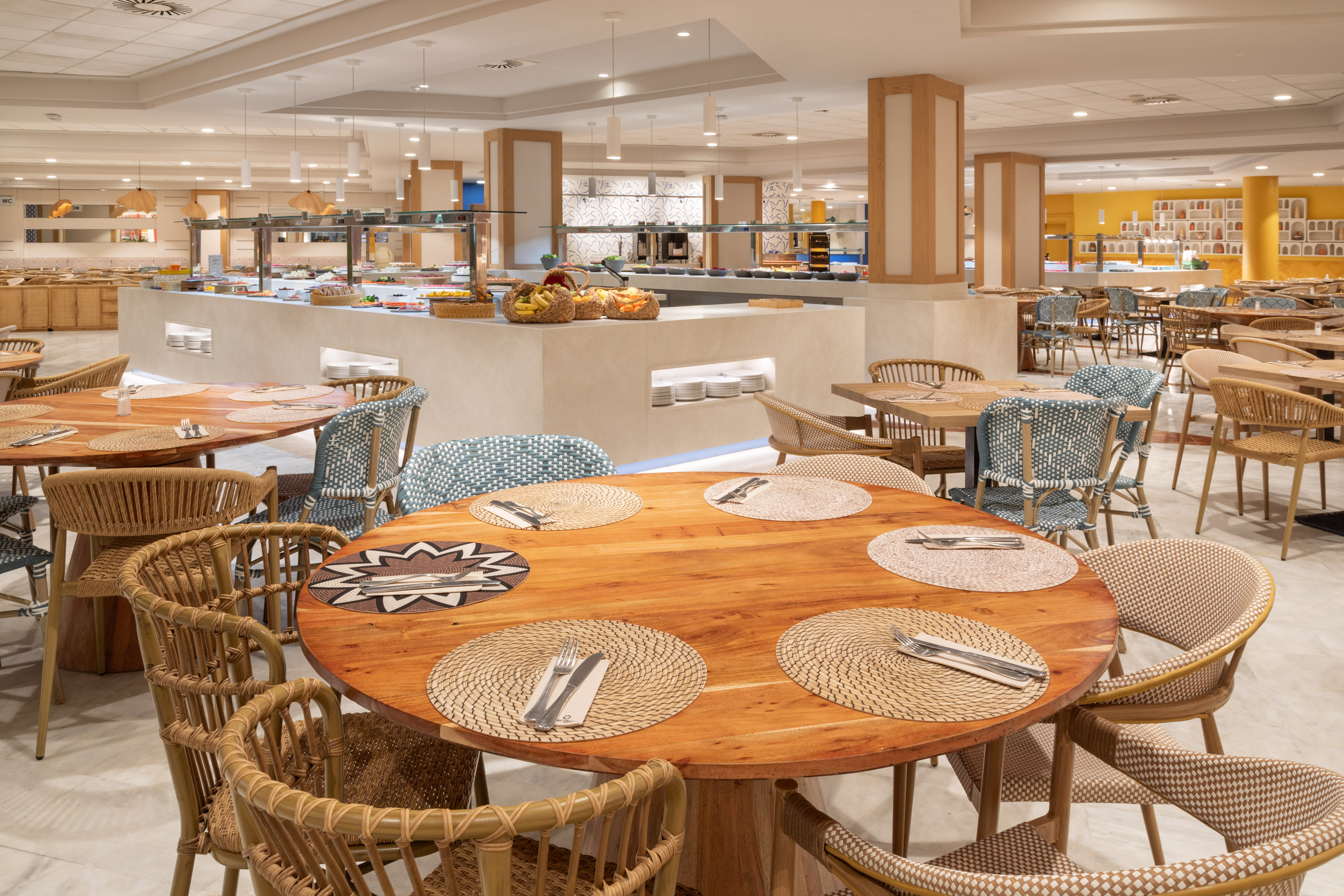 Spacious hotel buffet restaurant with wooden tables and woven chairs.