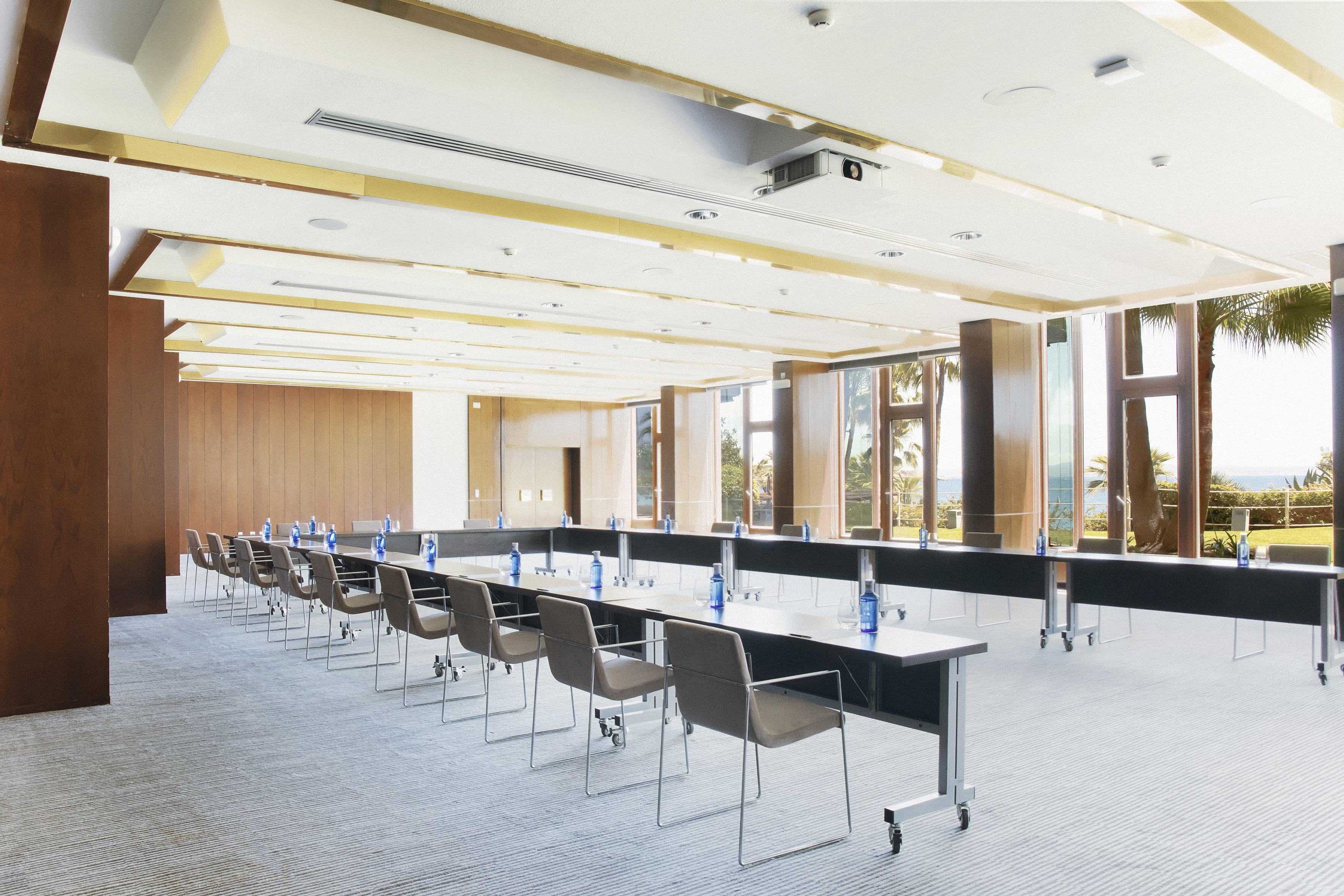Modern conference room with U-shaped table, projector, and ocean view through large windows.