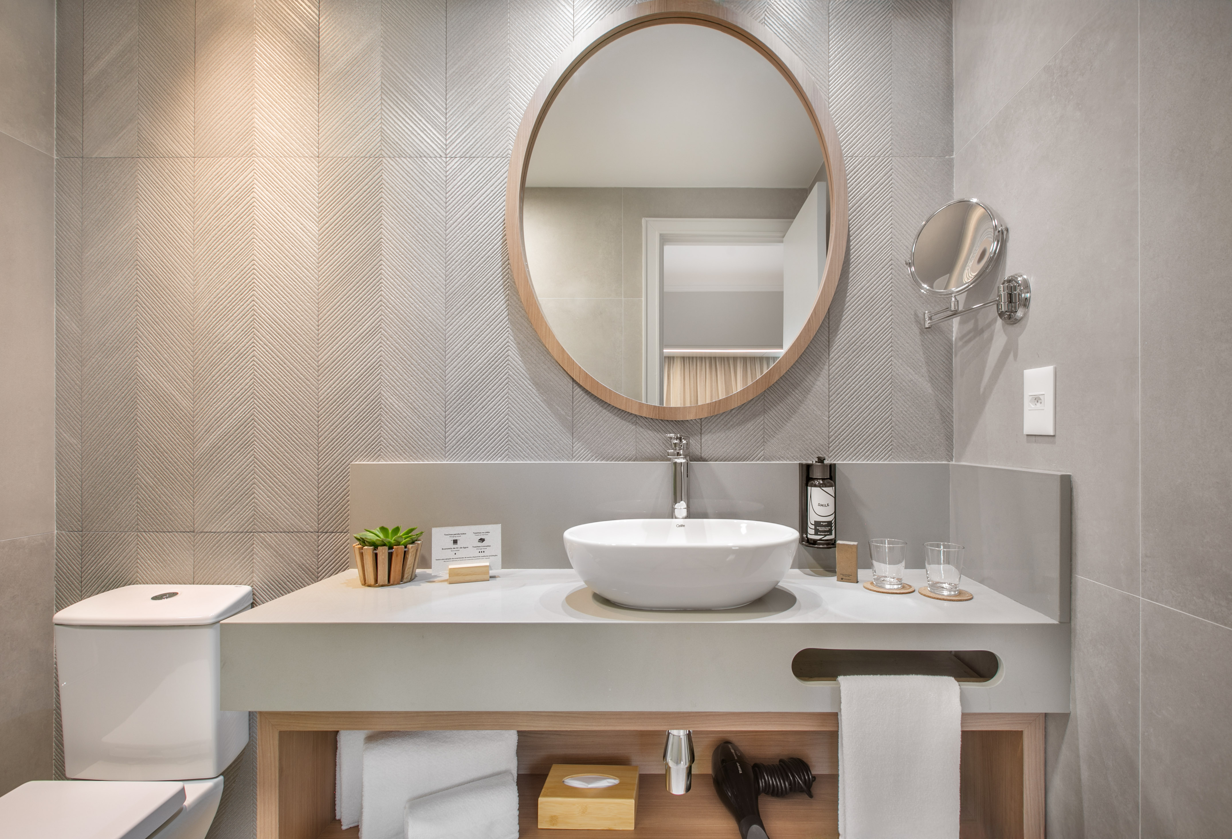 Modern bathroom with round mirror, white vessel sink, and grey patterned wall tiles.
