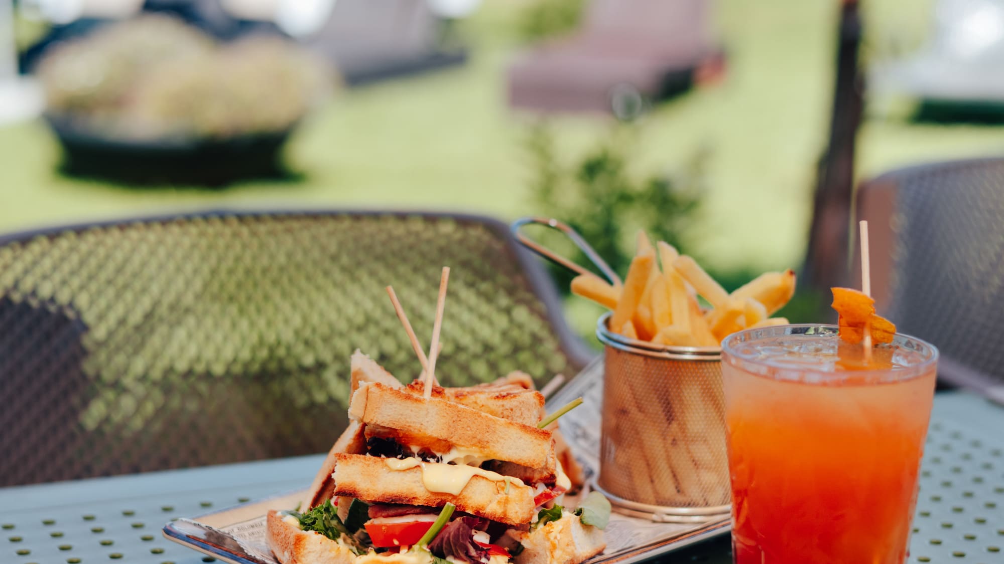 Club sandwich, fries, and cocktail on a table at an outdoor pool bar resort.