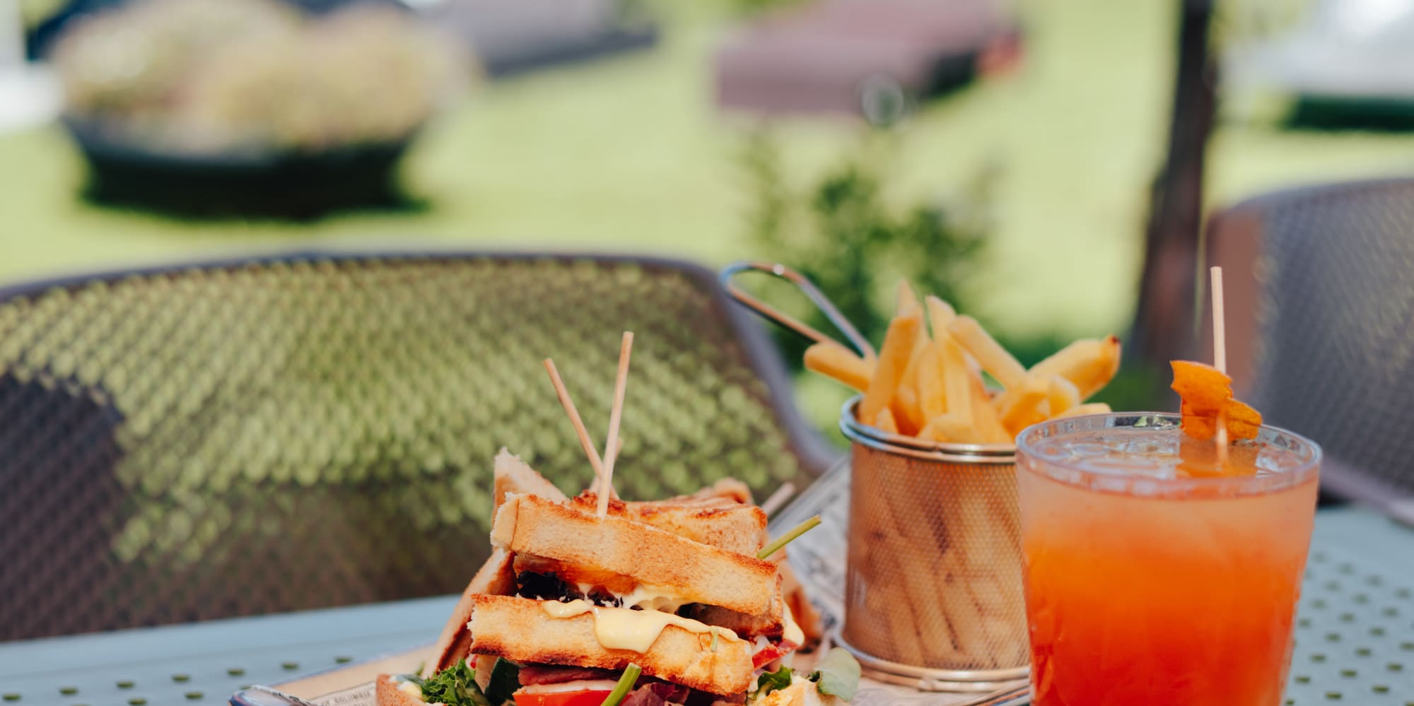 Club sandwich, fries, and cocktail on a table at an outdoor pool bar resort.