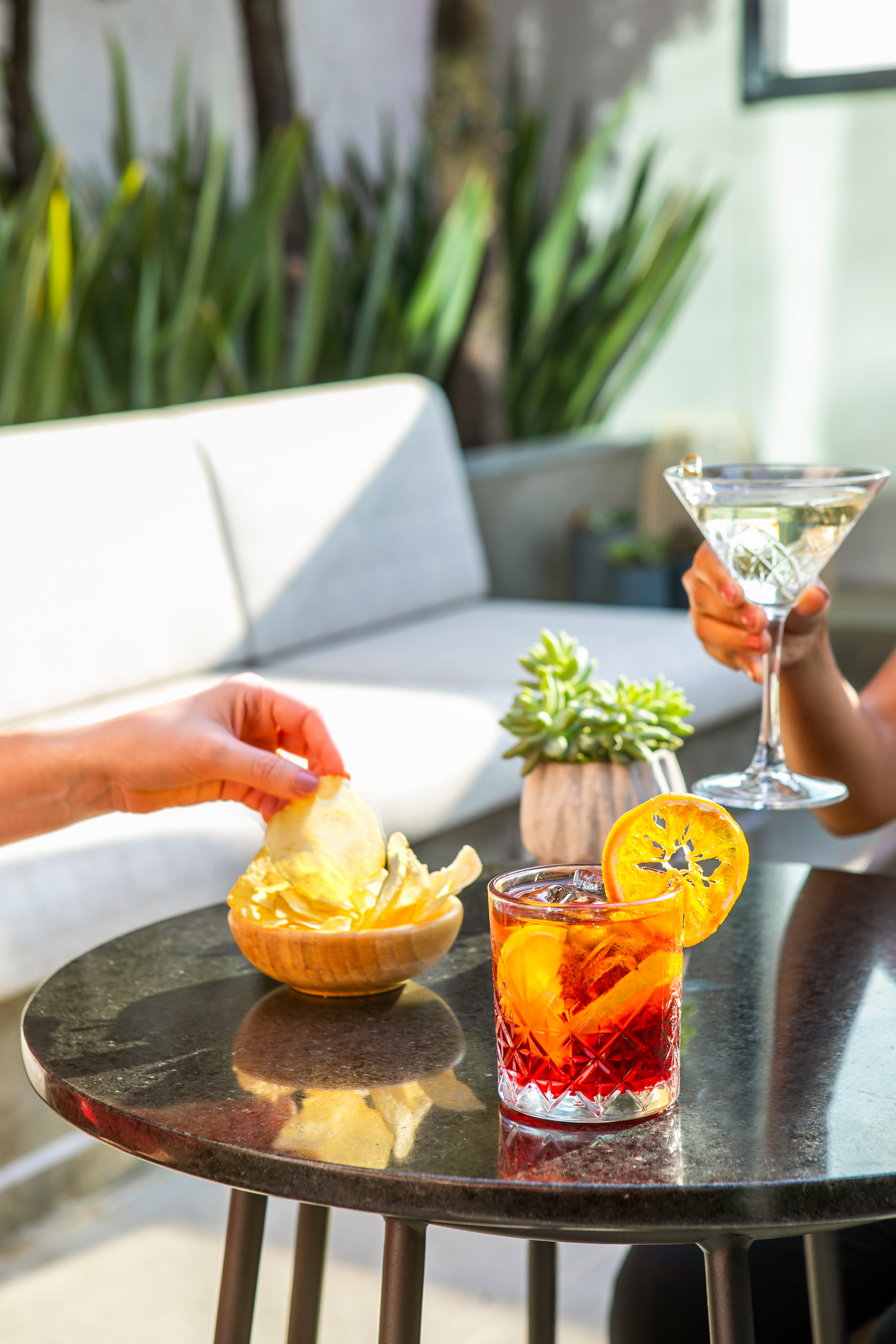 Guests enjoying a cocktail and martini with chips on an outdoor patio.