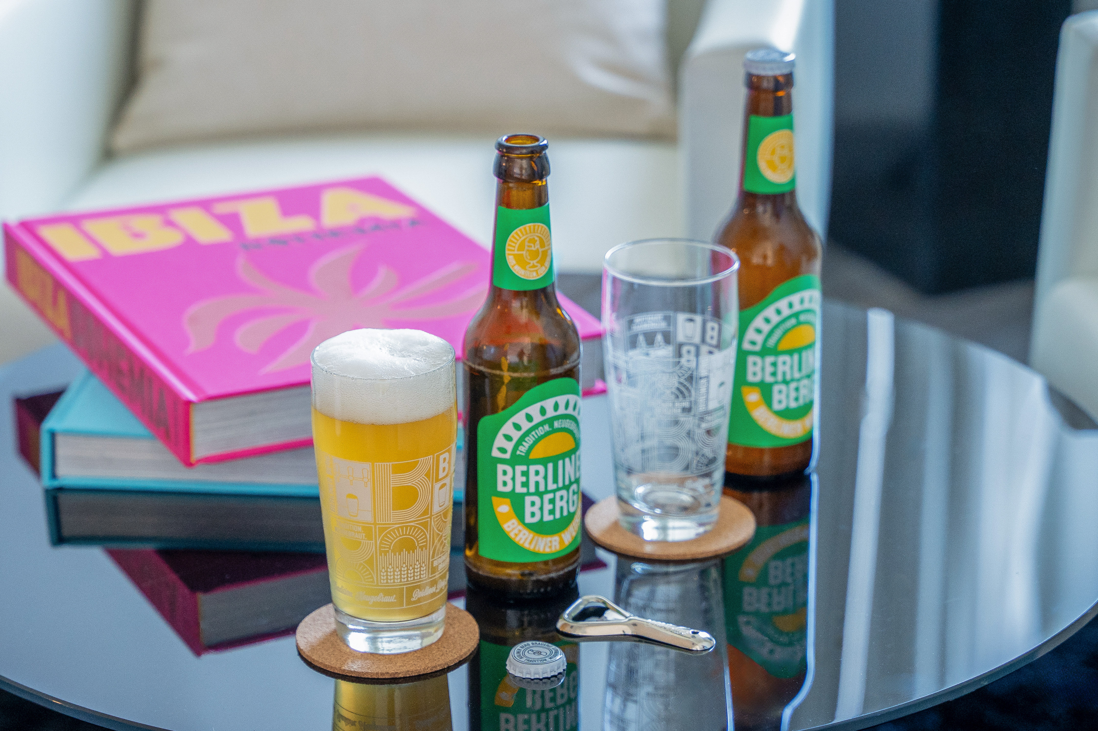 Berliner Berg bottles, foamy glass, opener on black table with IBIZA book.