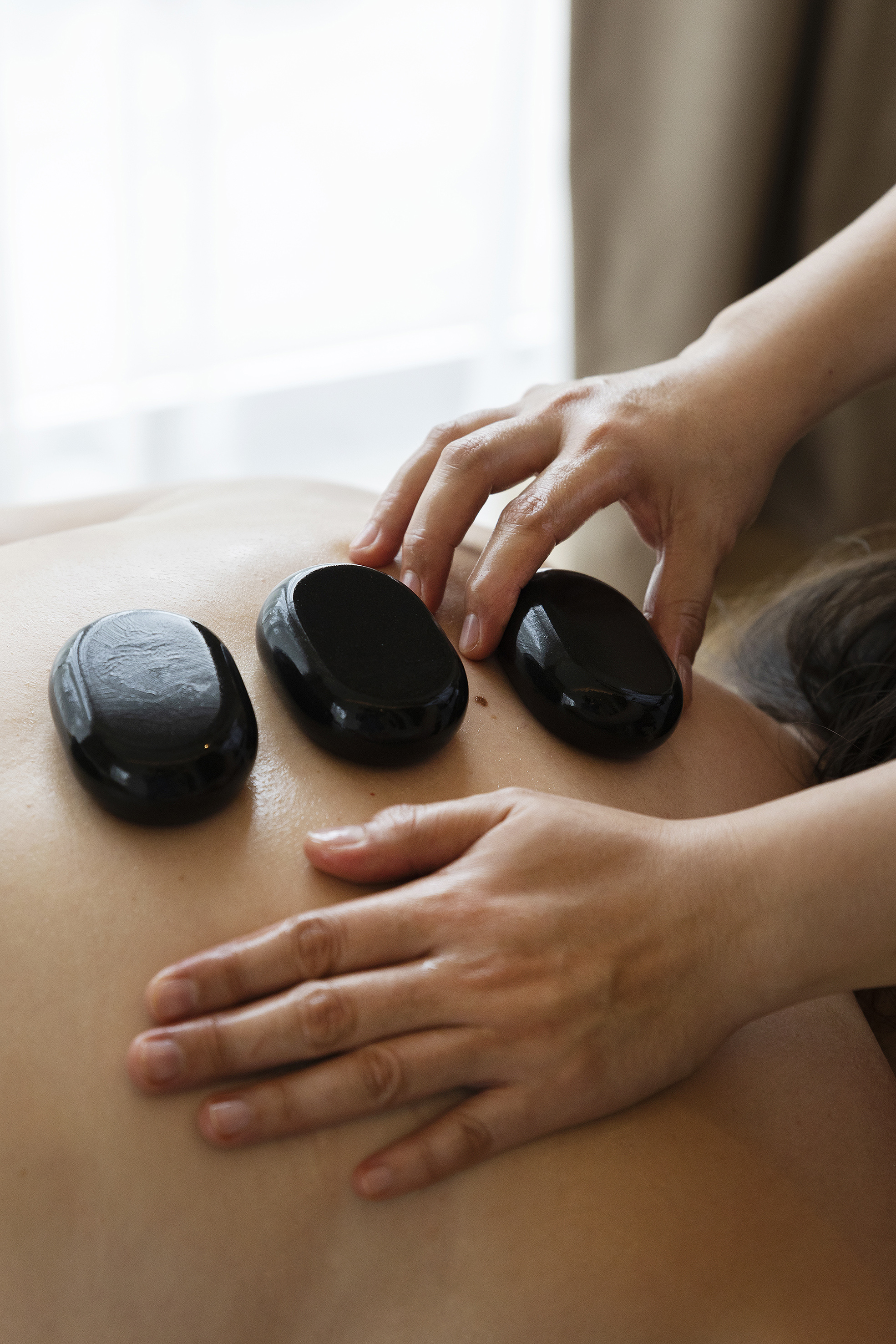 Spa hot stone massage on back, therapist hands placing smooth black stones.