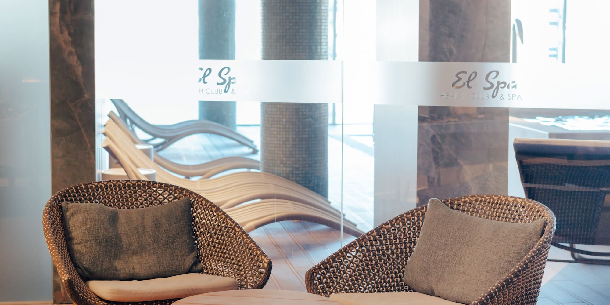El Spa health club lounge with woven chairs, wooden table, and jute rug.