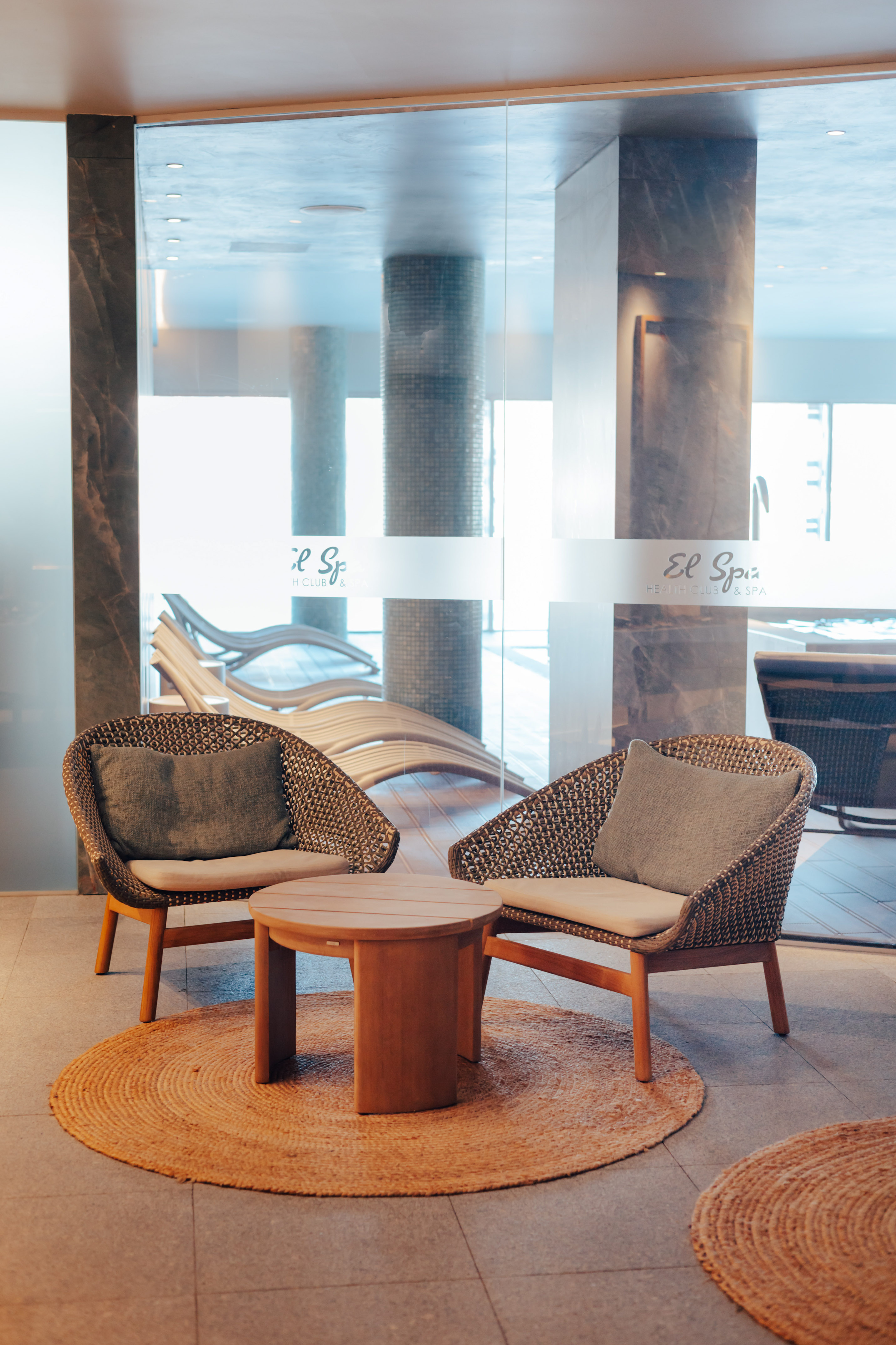 El Spa health club lounge with woven chairs, wooden table, and jute rug.