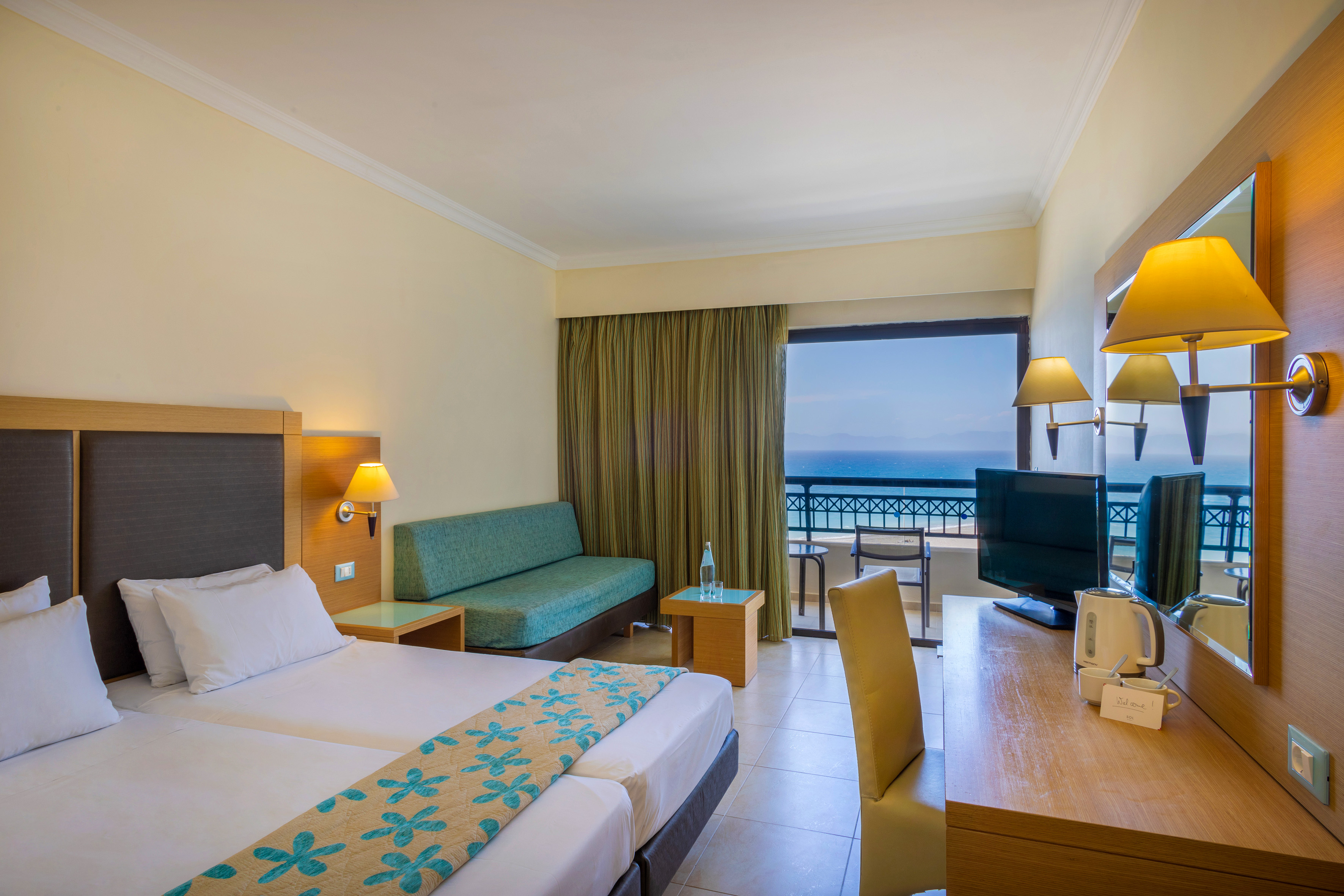 Hotel room with sea view balcony, double bed, sofa, and work desk.