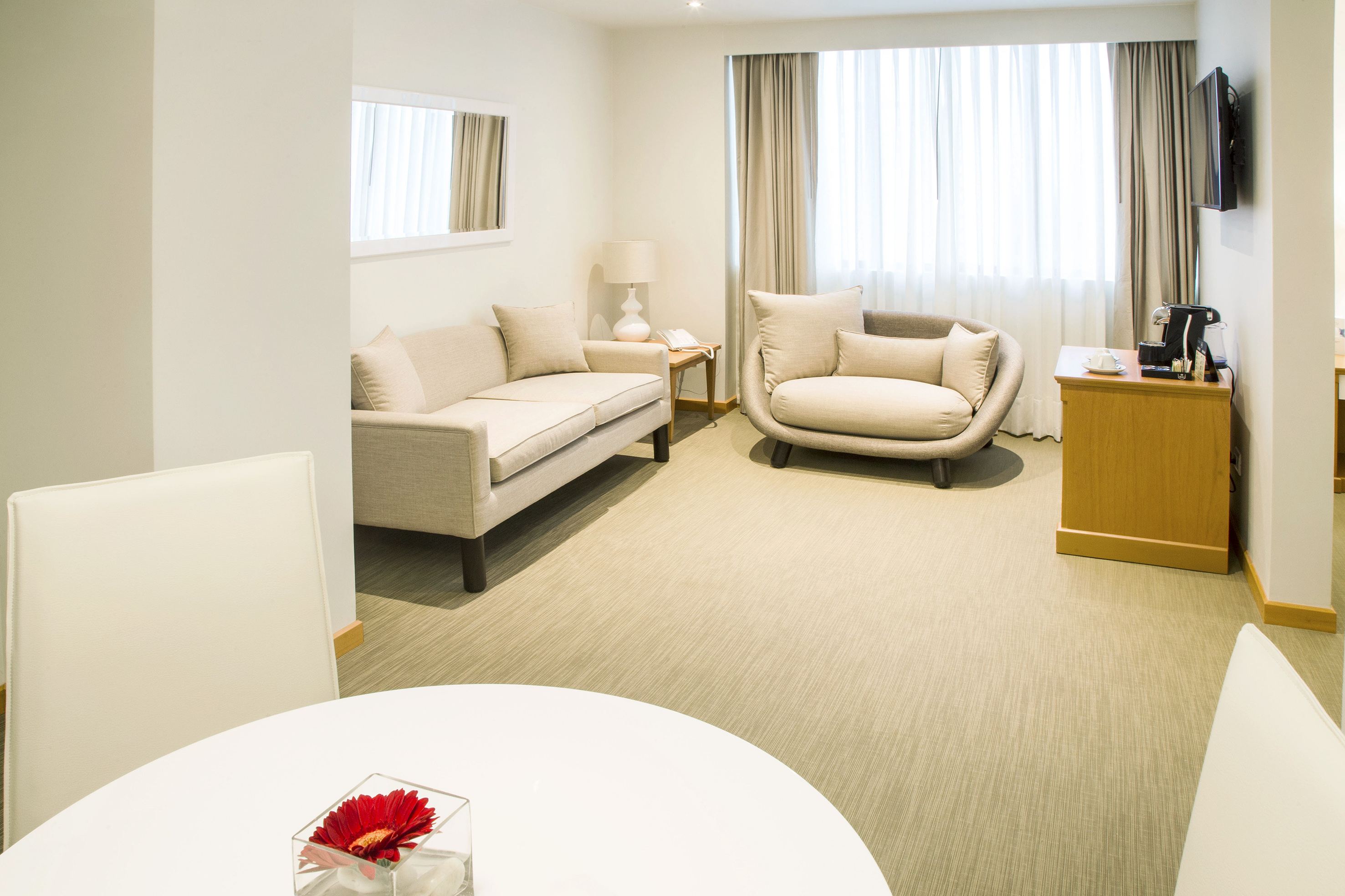 Hotel suite living area with beige sofas, large window, and coffee station.