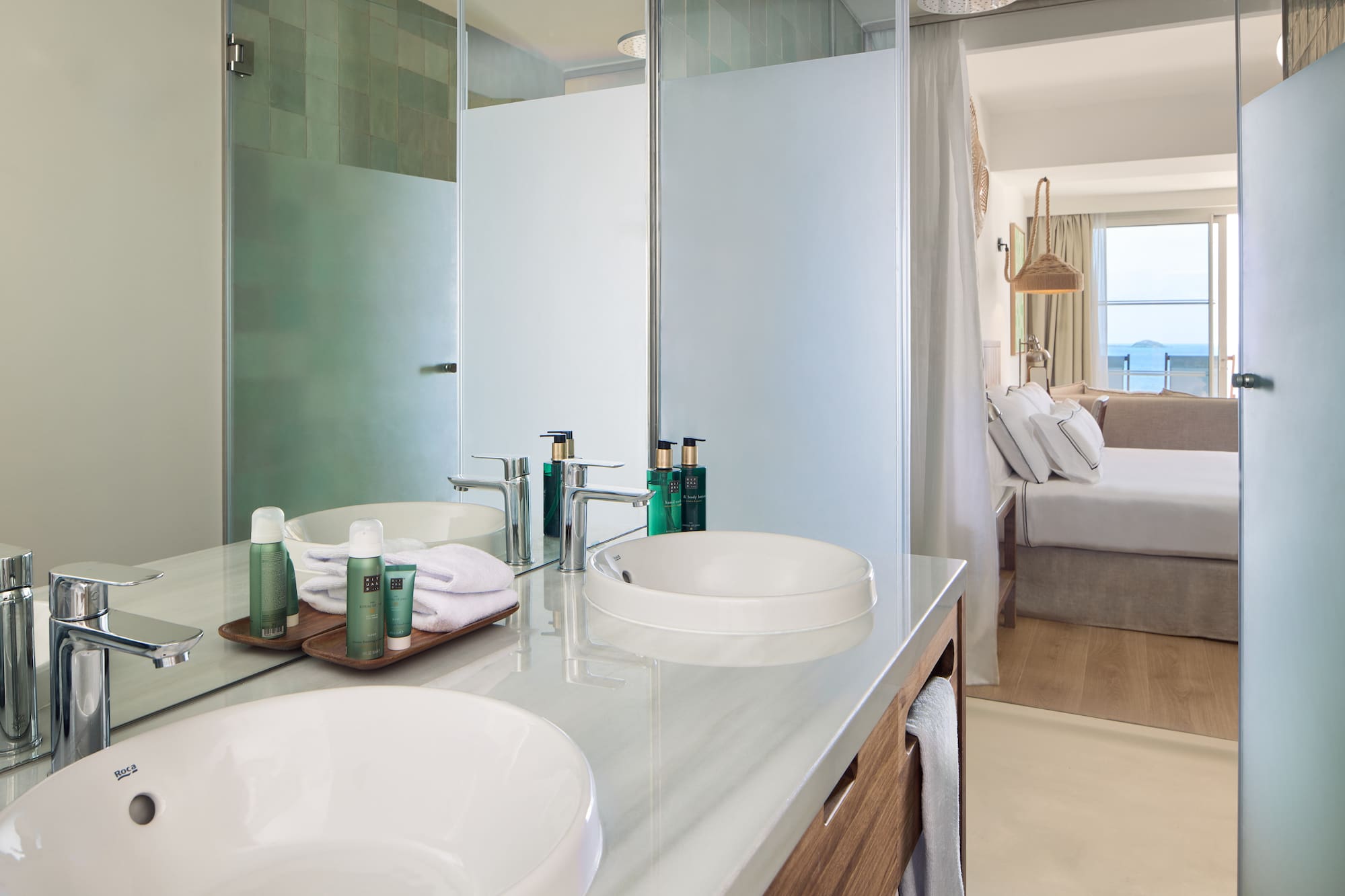 Modern hotel bathroom with double vanity, shower, and bedroom ocean view.