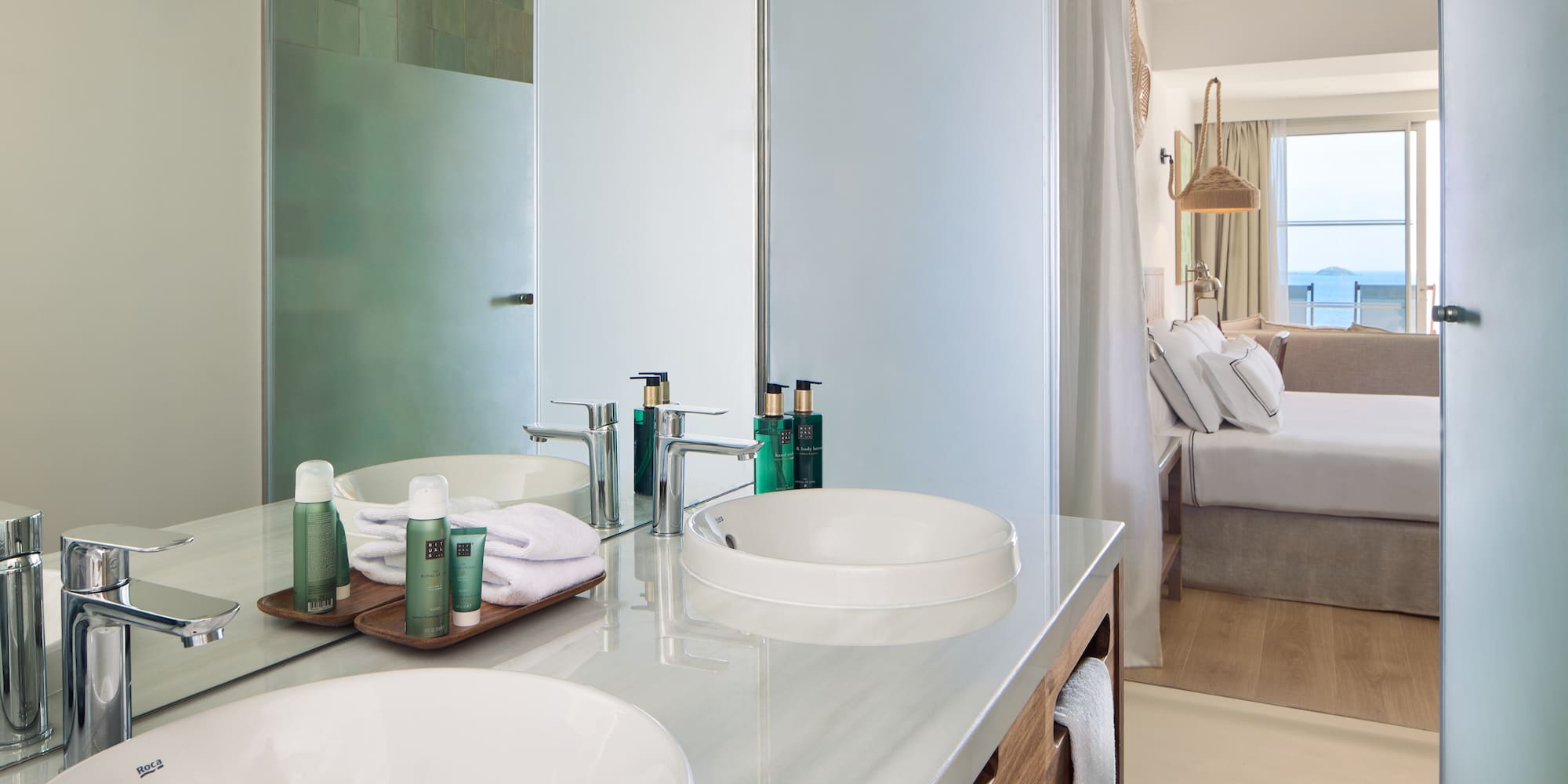 Modern hotel bathroom with double vanity, shower, and bedroom ocean view.