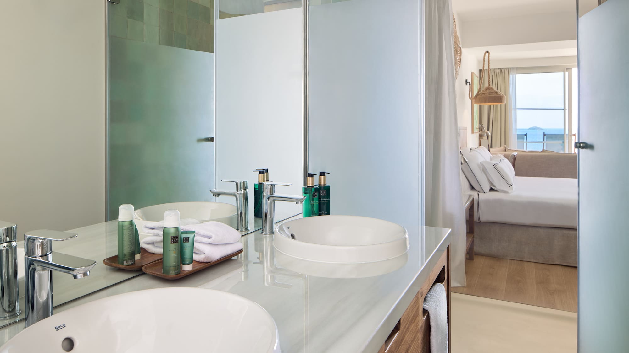 Modern hotel bathroom with double vanity, shower, and bedroom ocean view.