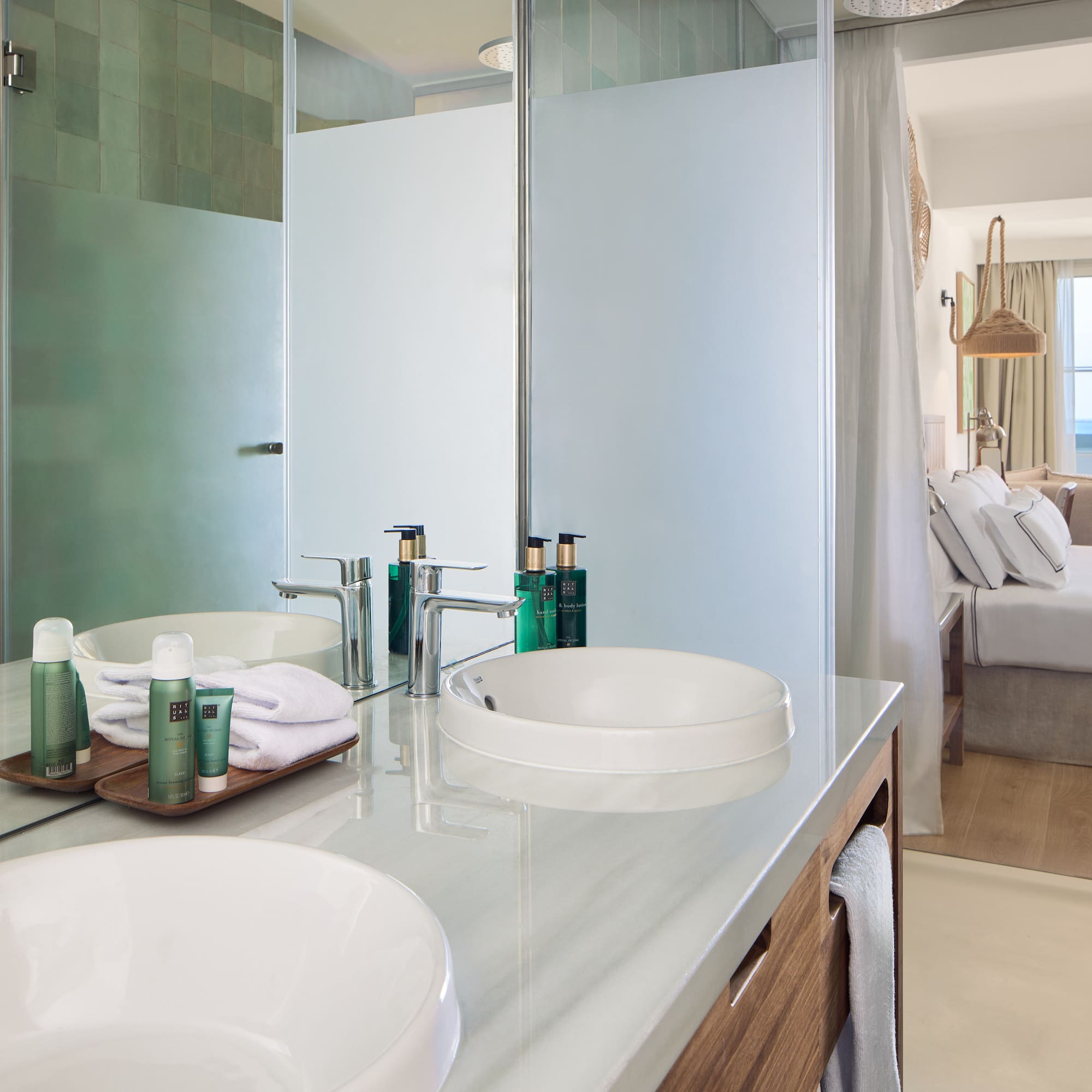 Modern hotel bathroom with double vanity, shower, and bedroom ocean view.