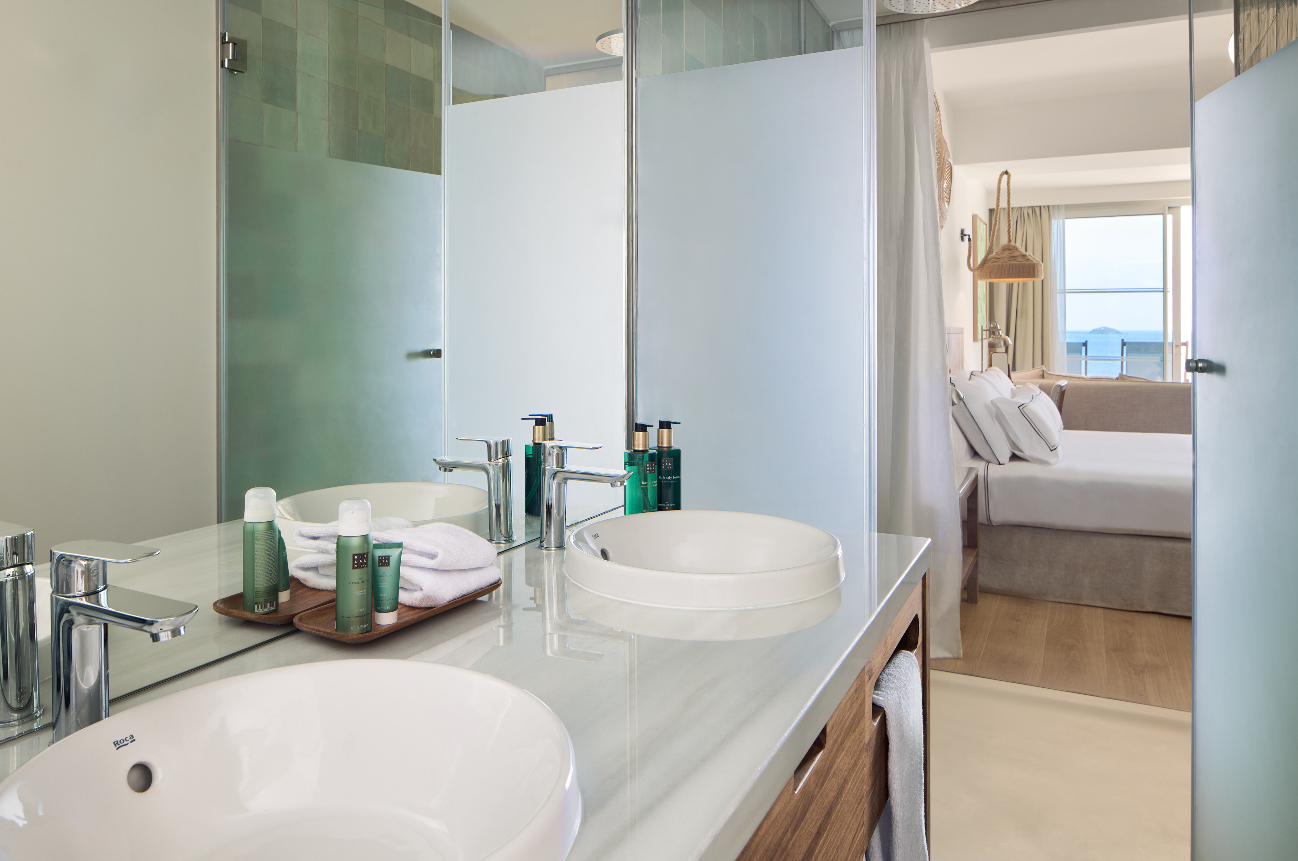 Modern hotel bathroom with double vanity, shower, and bedroom ocean view.