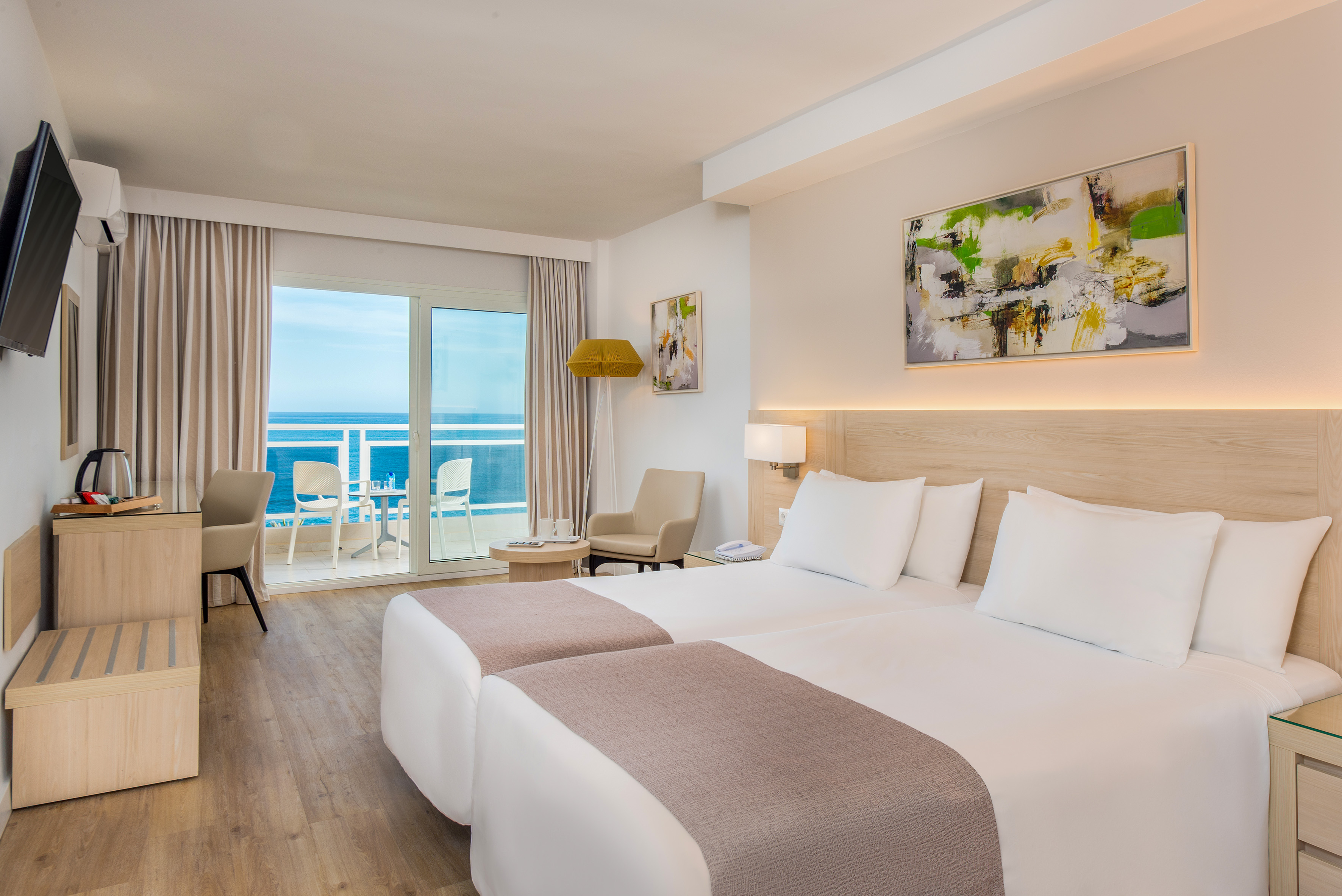 Modern hotel room with twin beds, ocean view balcony, and stylish decor.