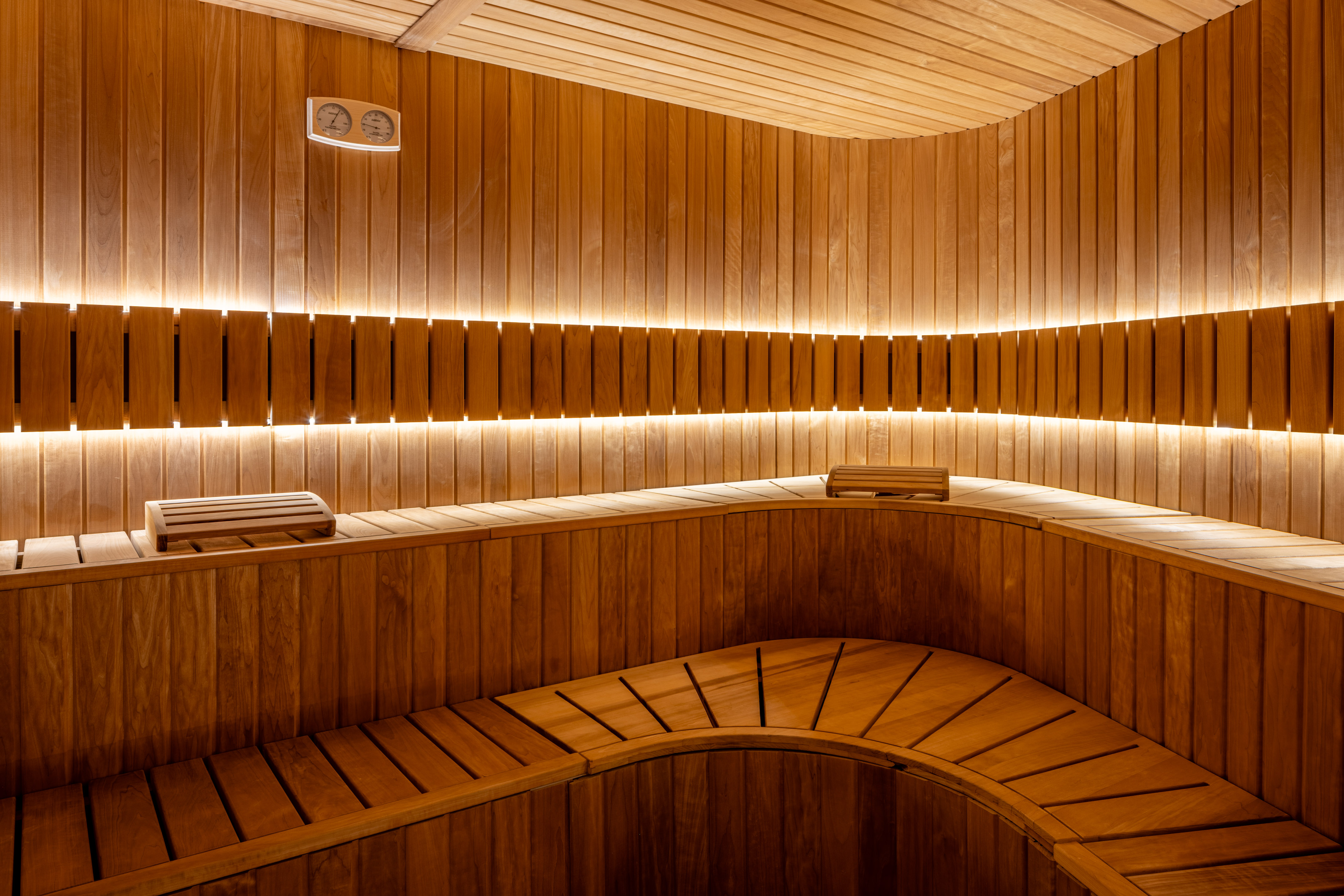 Modern wooden sauna interior with curved benches, LED lighting, and thermometer.