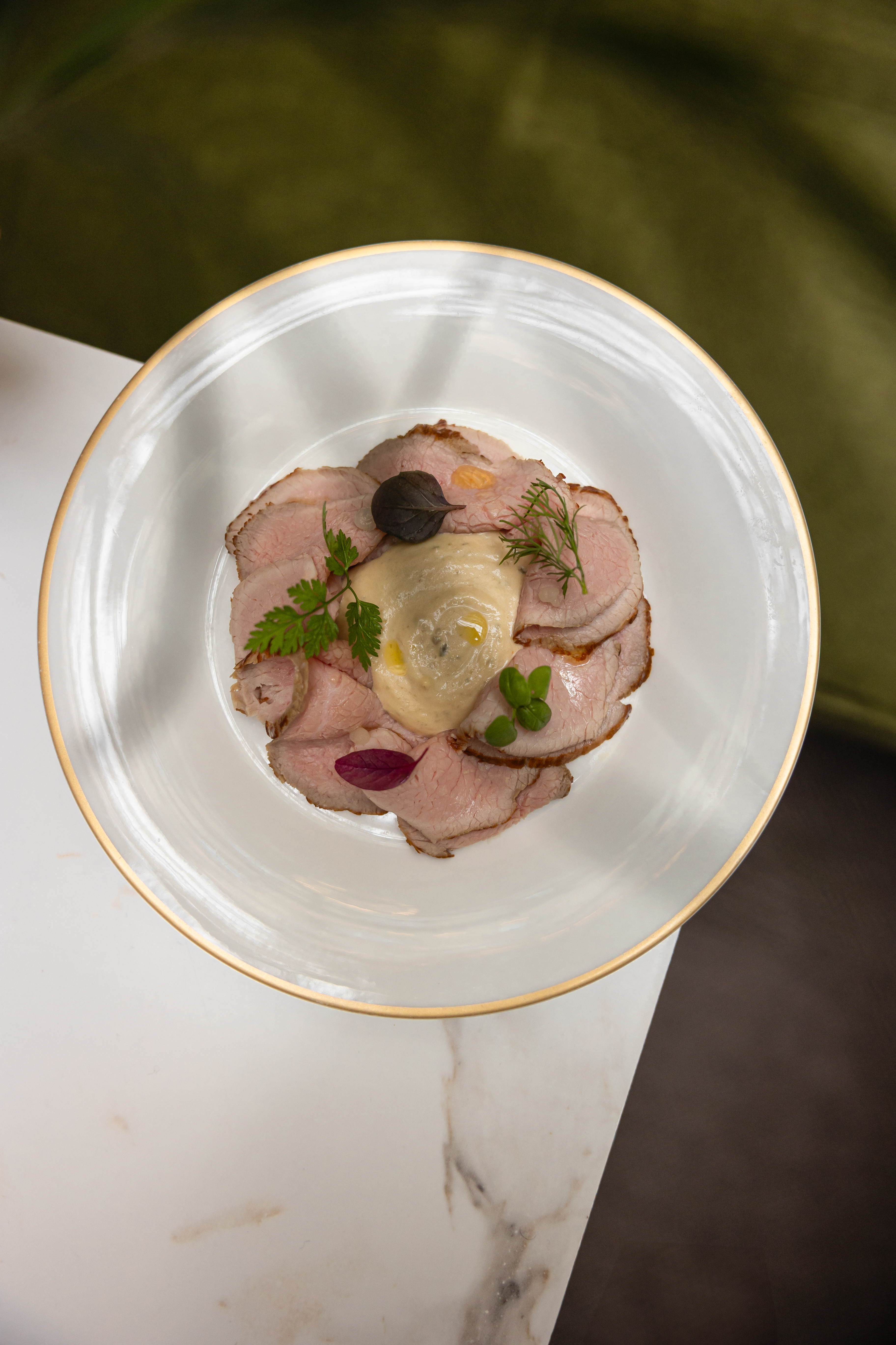 Sliced roast meat with creamy sauce and fresh herbs on a gold-rimmed plate.