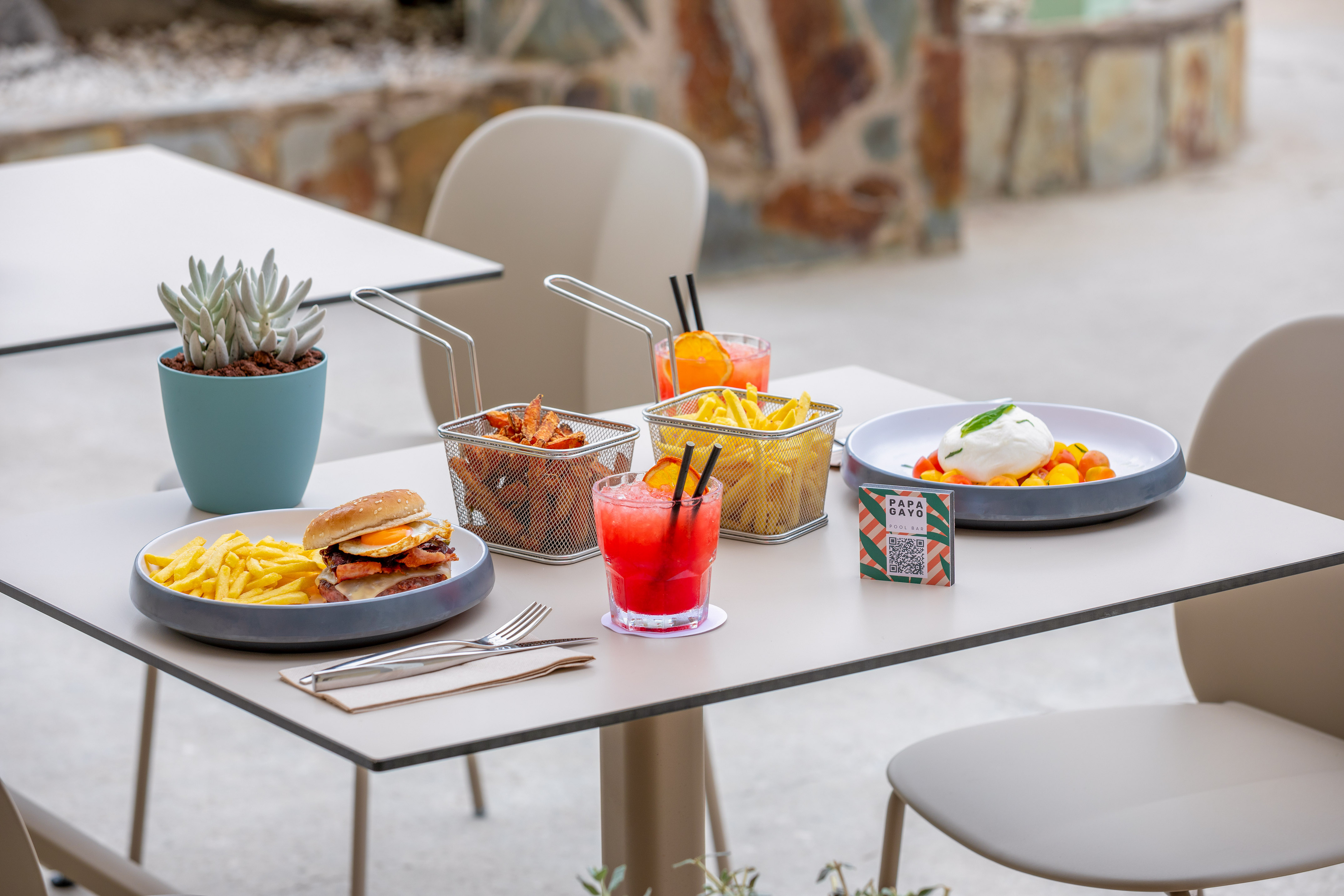 Outdoor table with burger, fries, sweet potato fries, burrata, and cocktails.