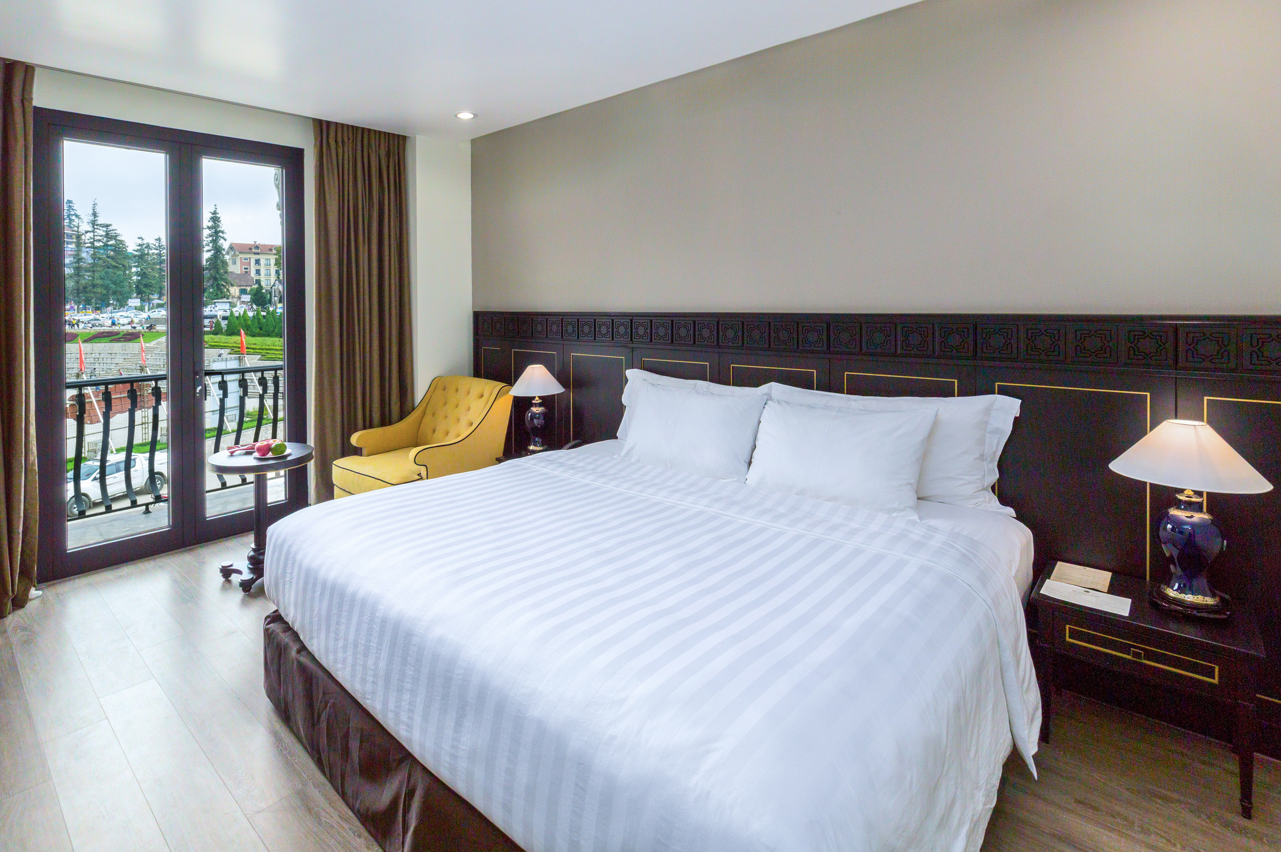 Modern hotel bedroom with white king bed, balcony, and yellow armchair.