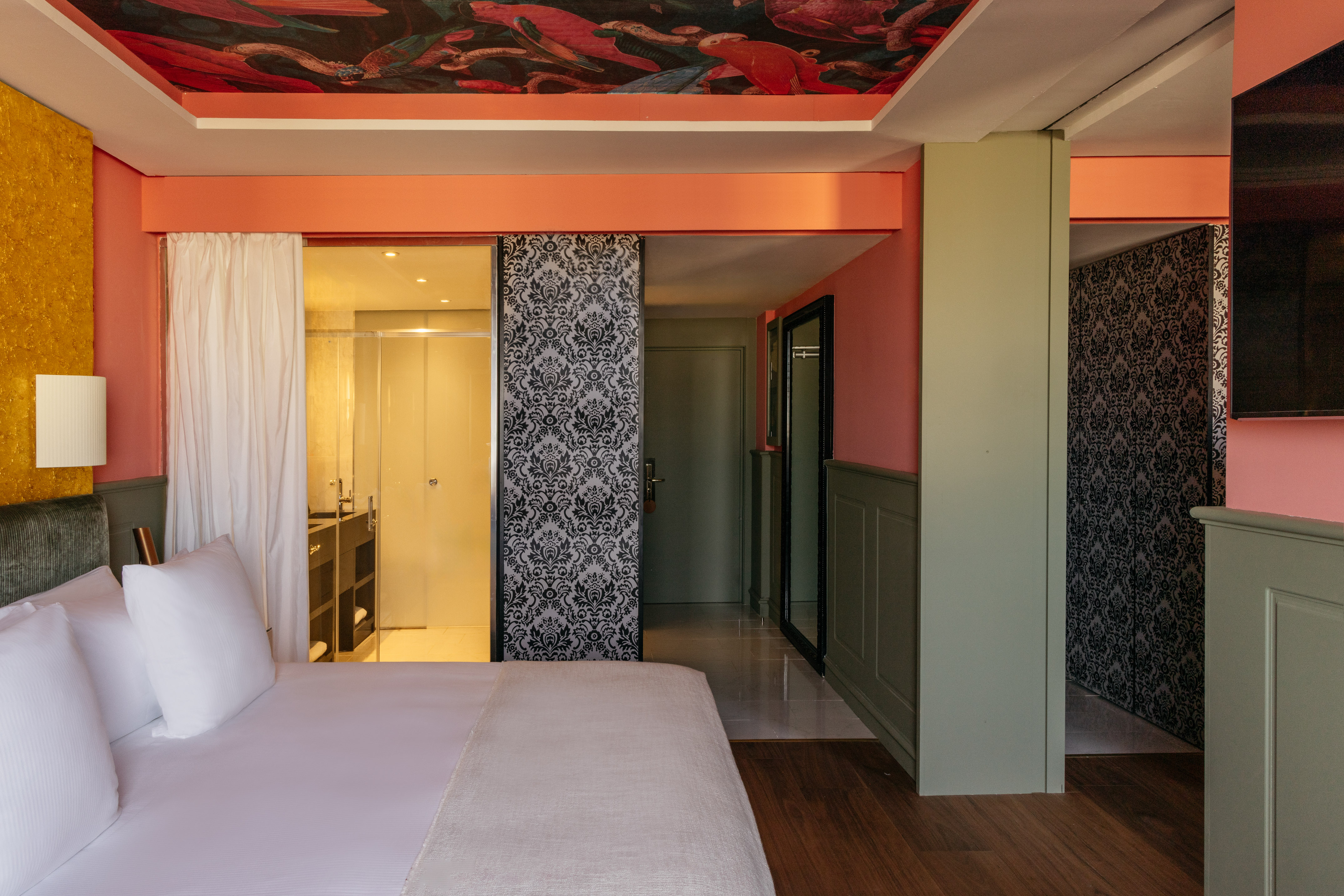 Vibrant hotel bedroom with coral walls, colorful ceiling mural, and modern interior.