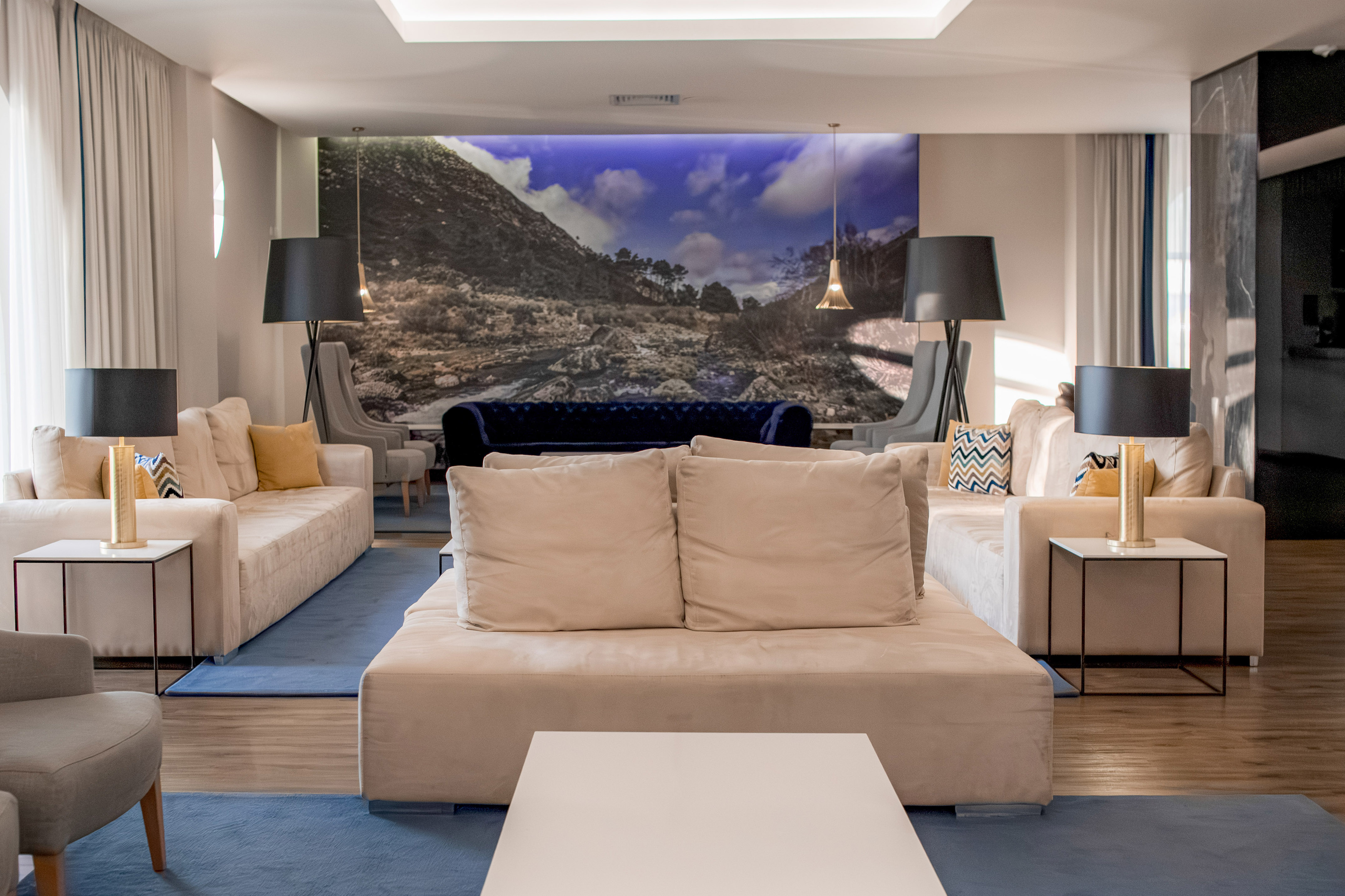 Modern hotel lobby with beige sofas, blue rug, and large landscape wall mural.