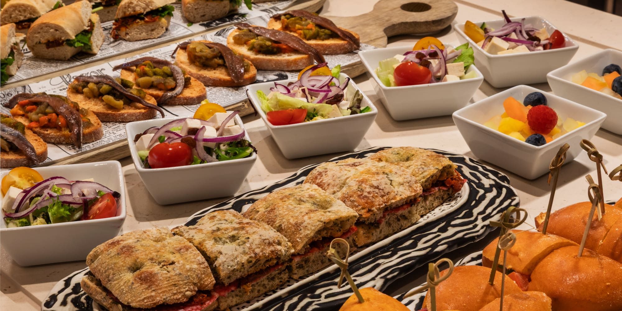 Mesa de catering con pinchos, bocadillos, ensaladas y fruta fresca.