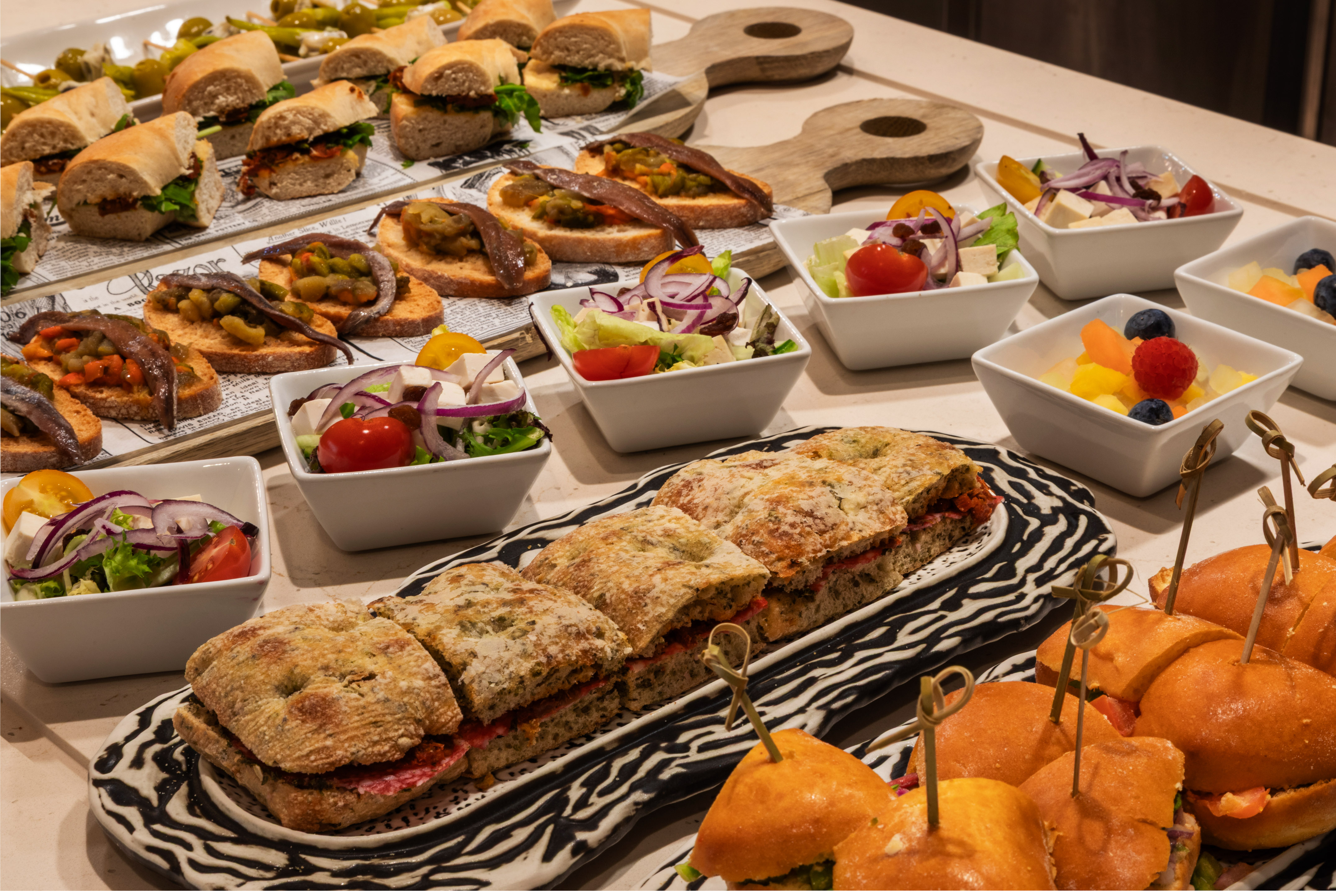 Mesa de catering con pinchos, bocadillos, ensaladas y fruta fresca.