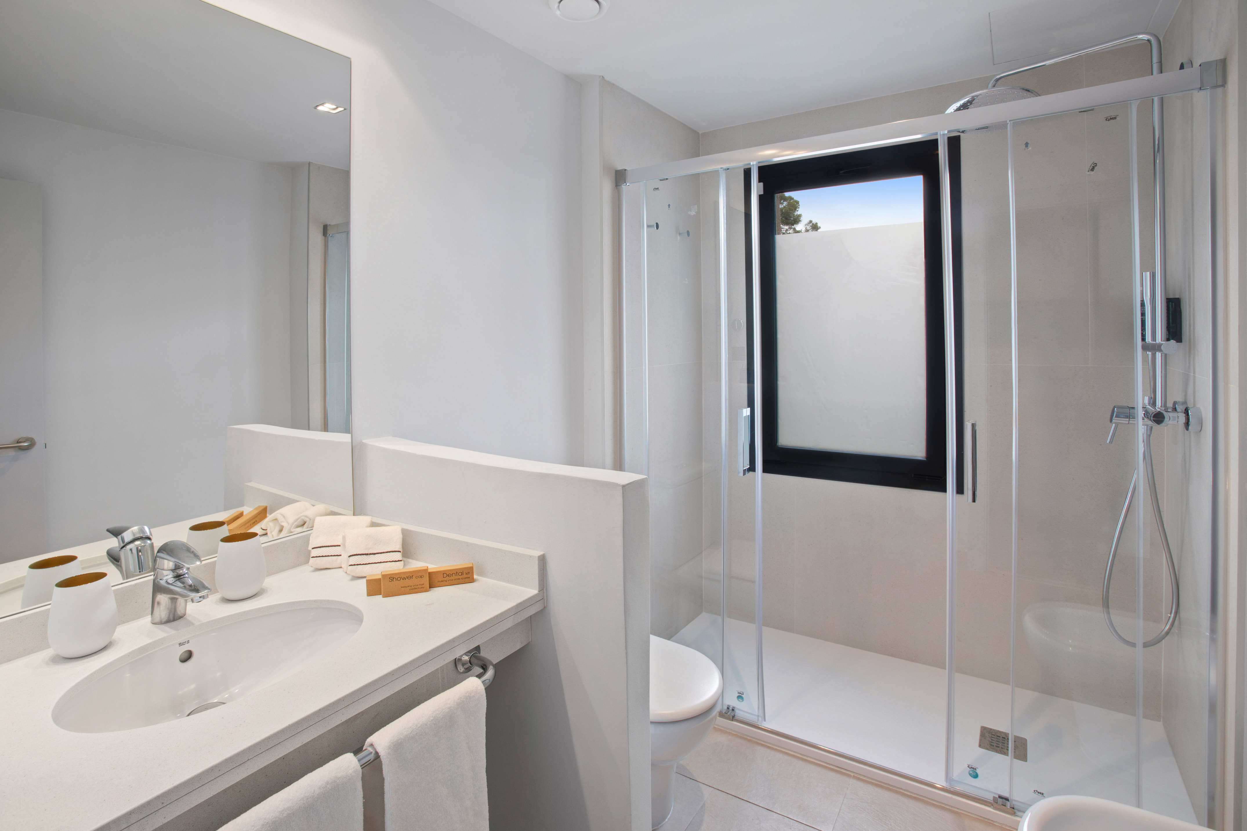 Bright modern bathroom with white vanity, sink, mirror, and glass shower.