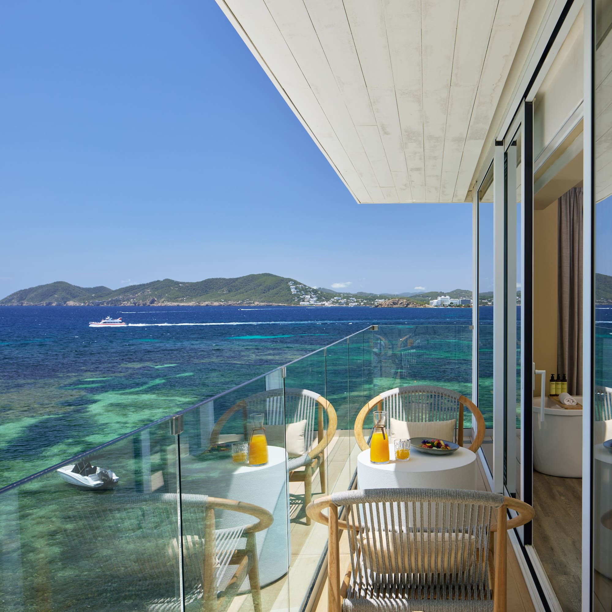 Hotel balcony with ocean view, breakfast on tables, and clear turquoise sea.