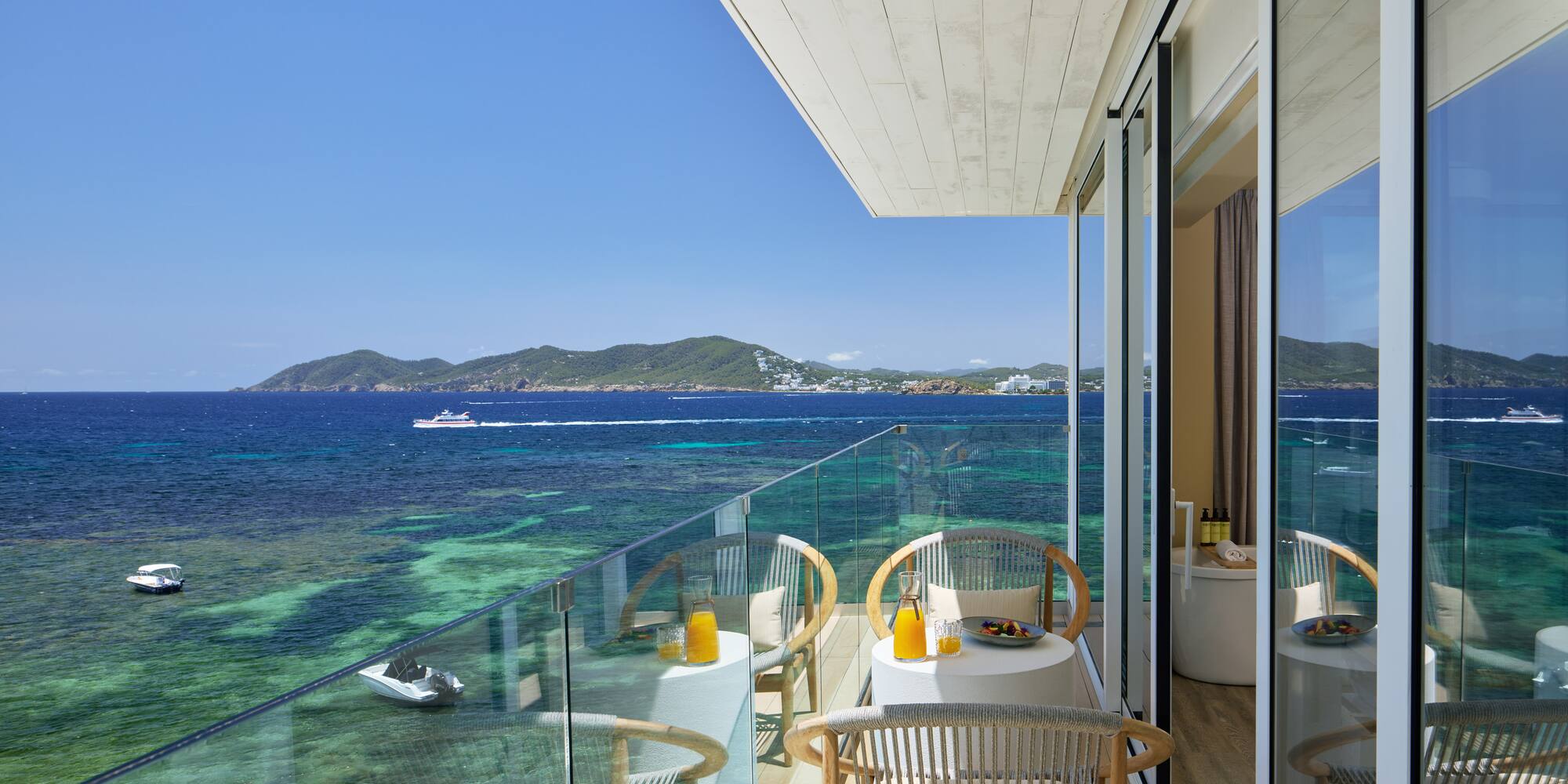Hotel balcony with ocean view, breakfast on tables, and clear turquoise sea.