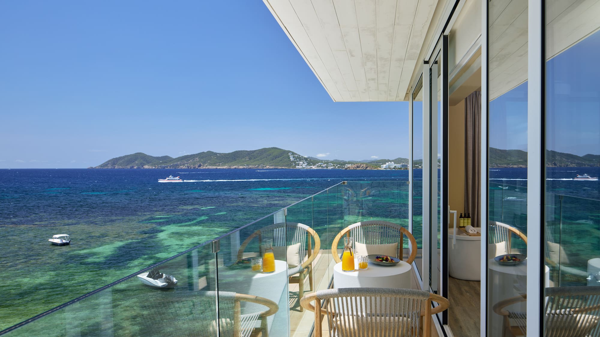 Hotel balcony with ocean view, breakfast on tables, and clear turquoise sea.
