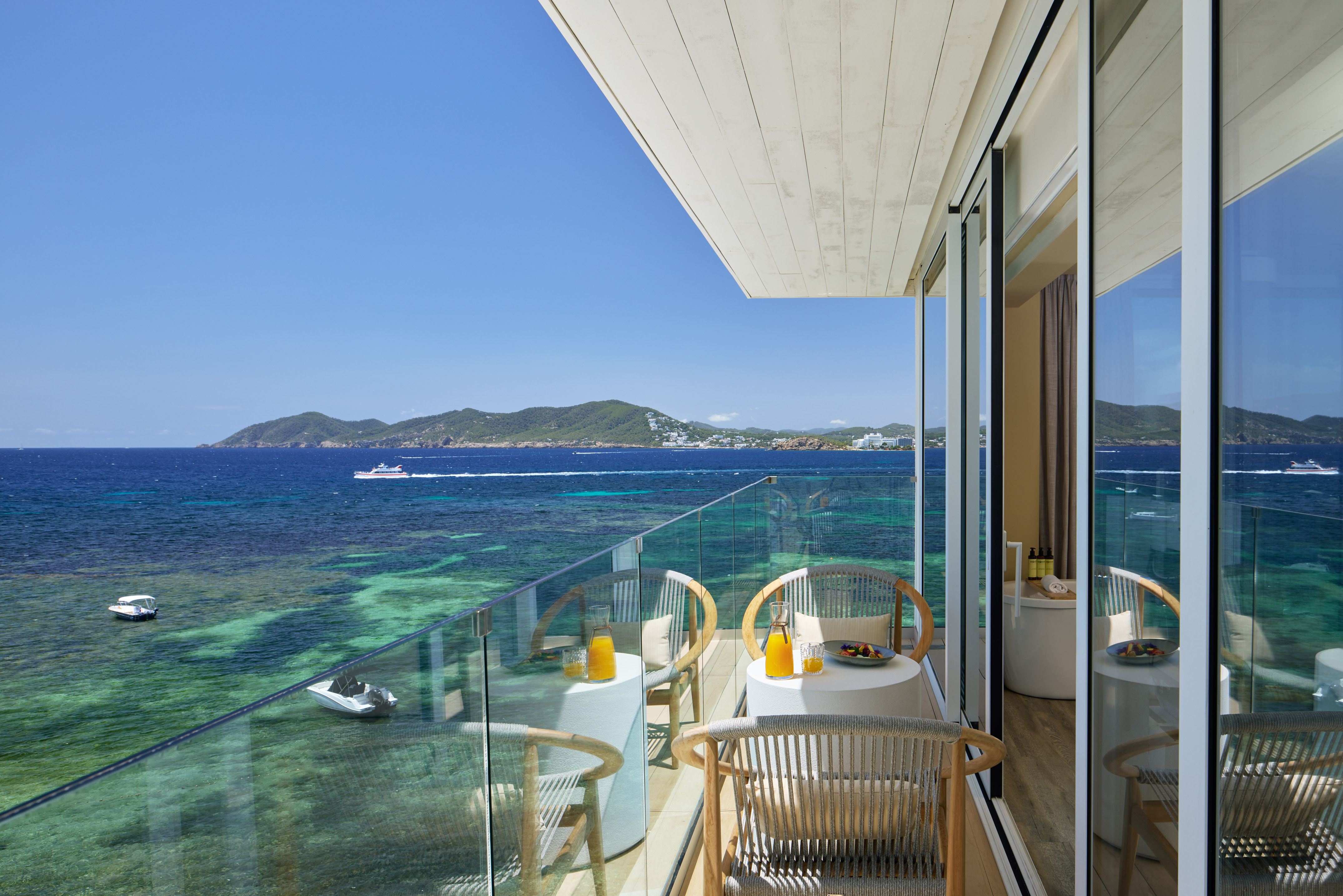 Hotel balcony with ocean view, breakfast on tables, and clear turquoise sea.