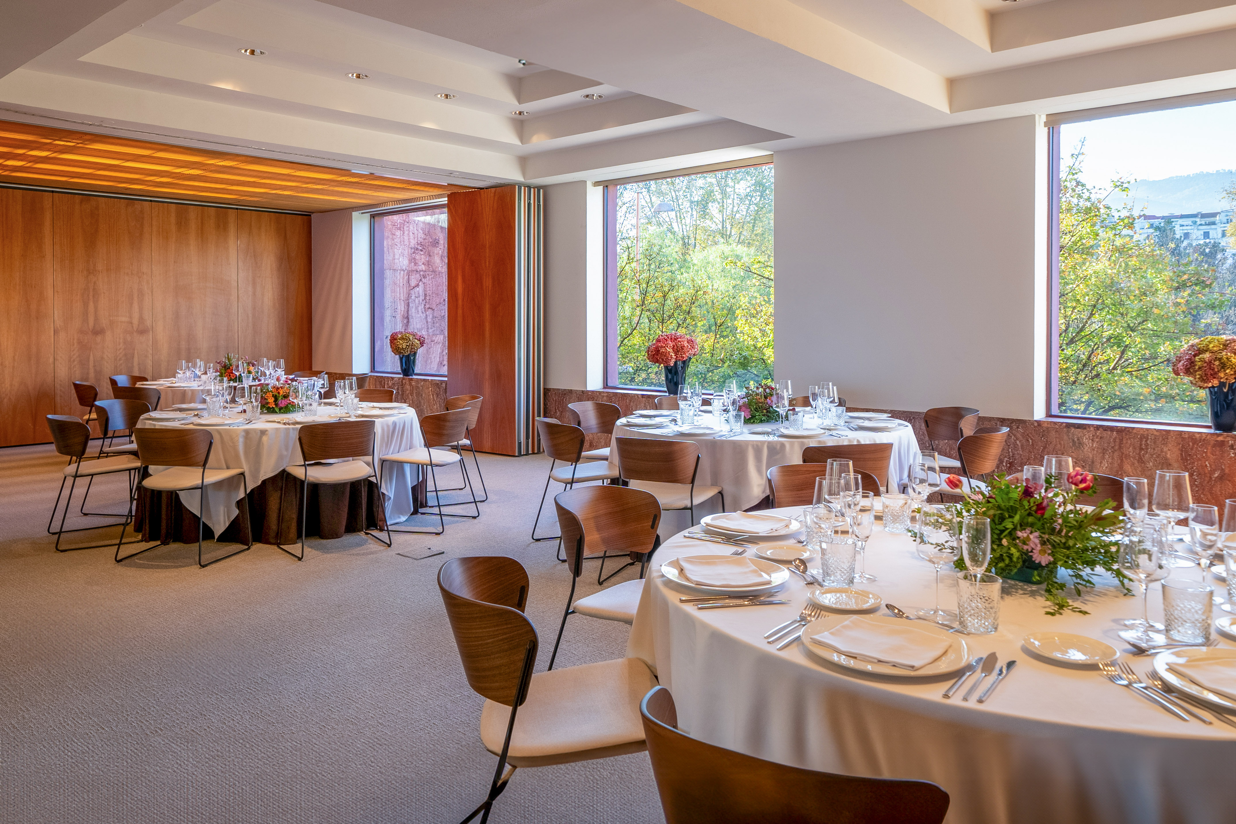 Modern event space with set round dining tables, chairs, and scenic windows.