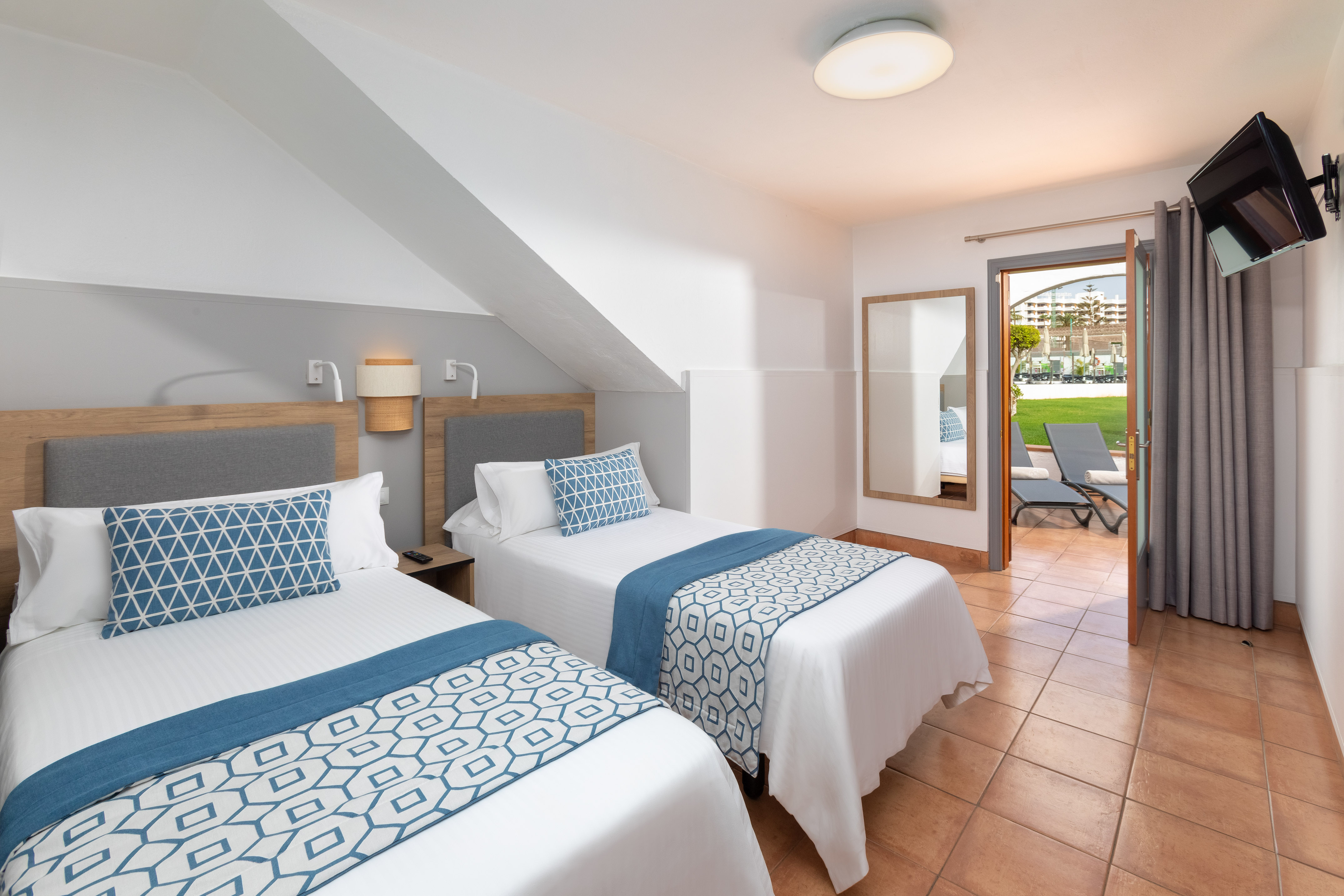 Twin hotel room with blue bedding, patio access, and garden view.