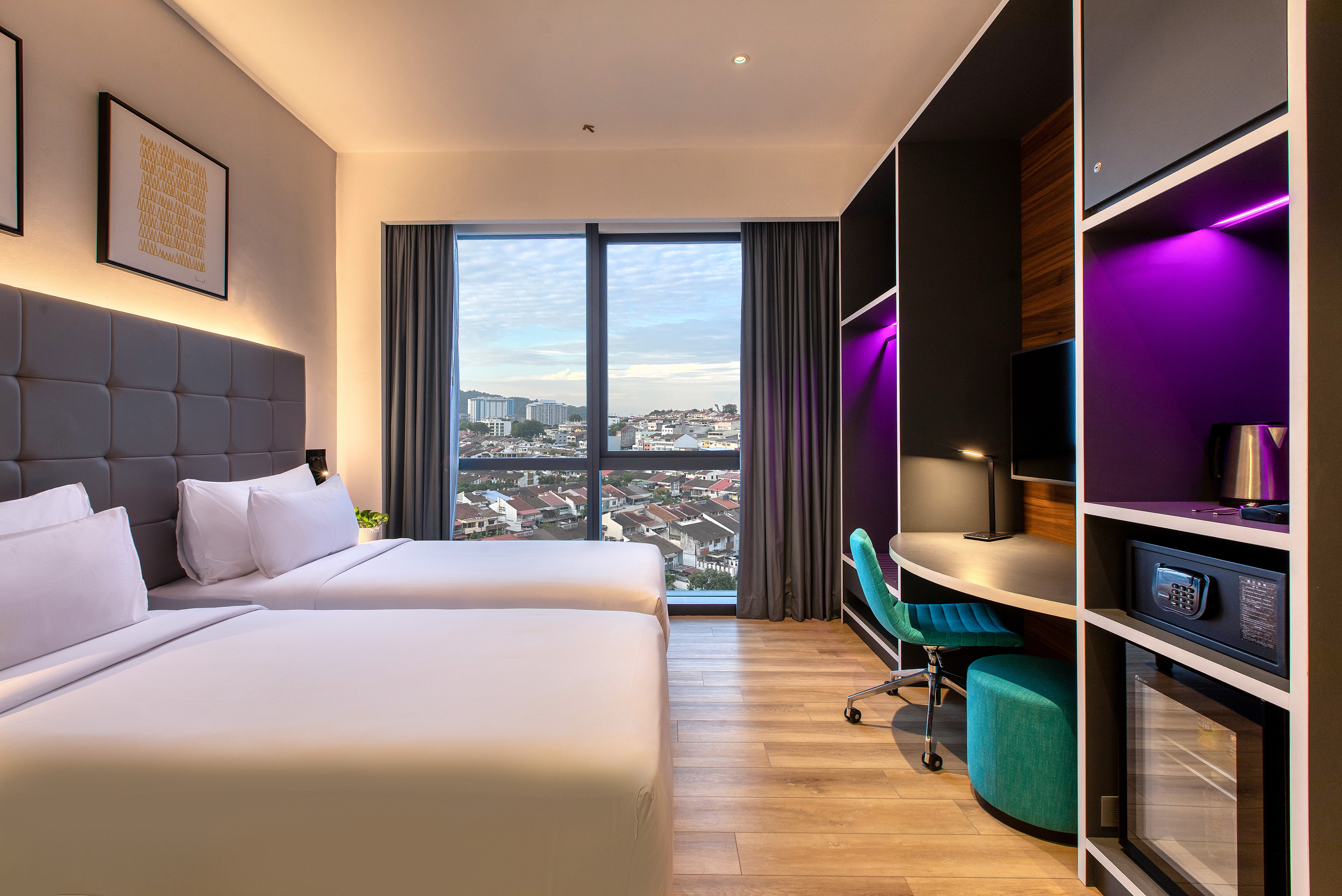 Modern hotel room with twin beds, city view, desk, and purple lit shelves.