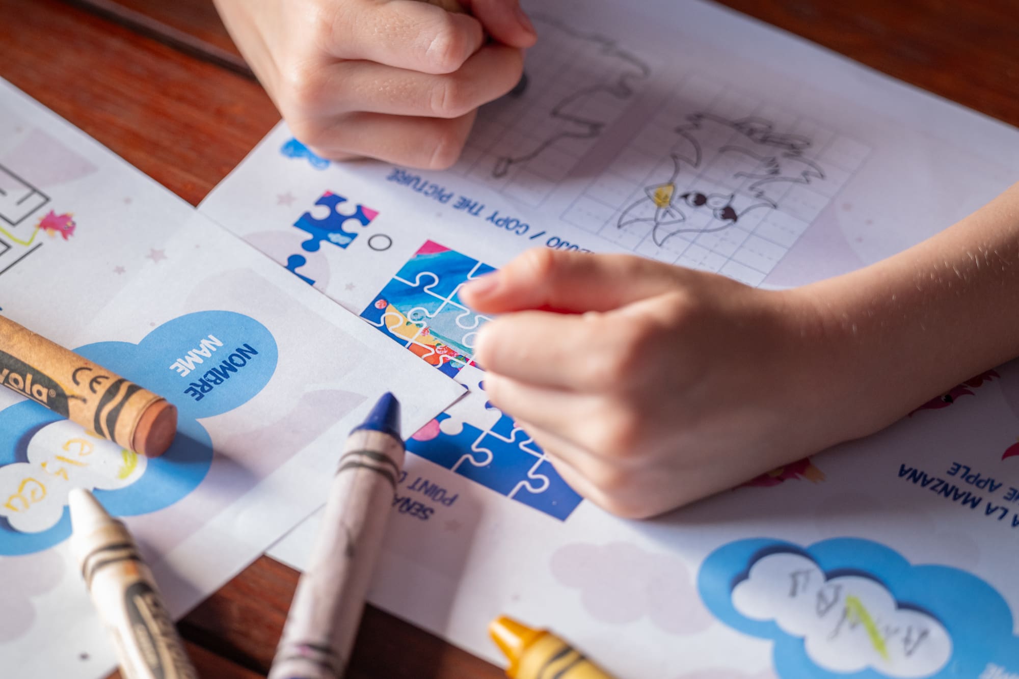 Manos de niño dibujando con crayones en hojas de actividades educativas.